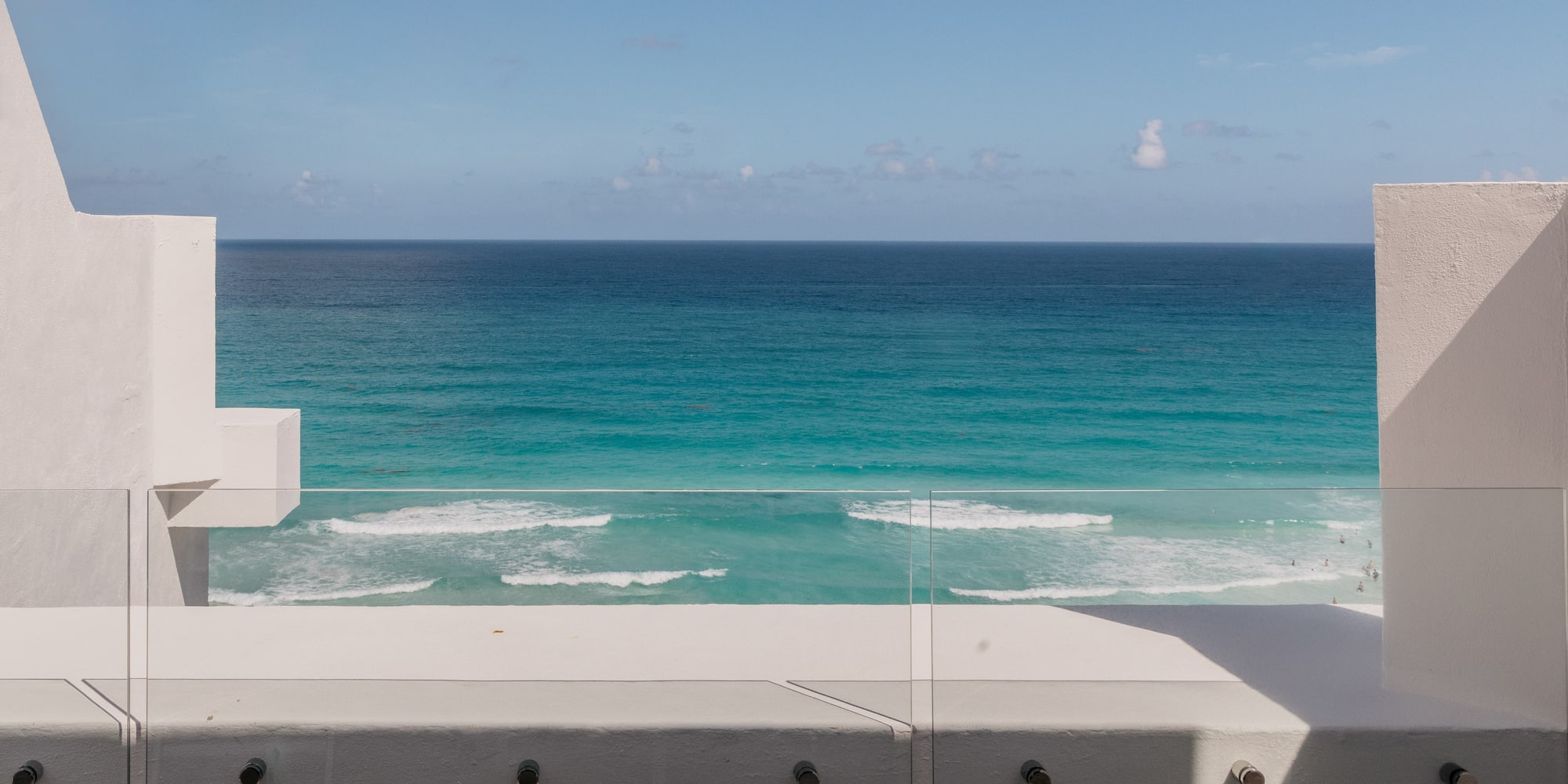 Modern balcony with glass railing, turquoise ocean view, and blue sky.