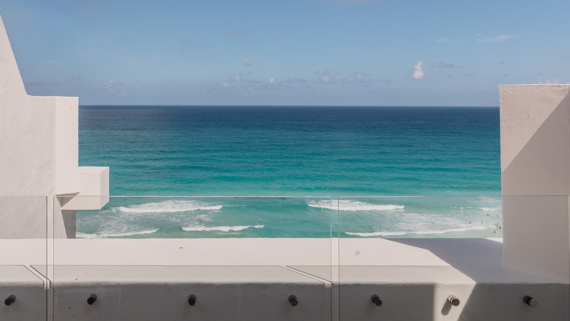 Modern balcony with glass railing, turquoise ocean view, and blue sky.