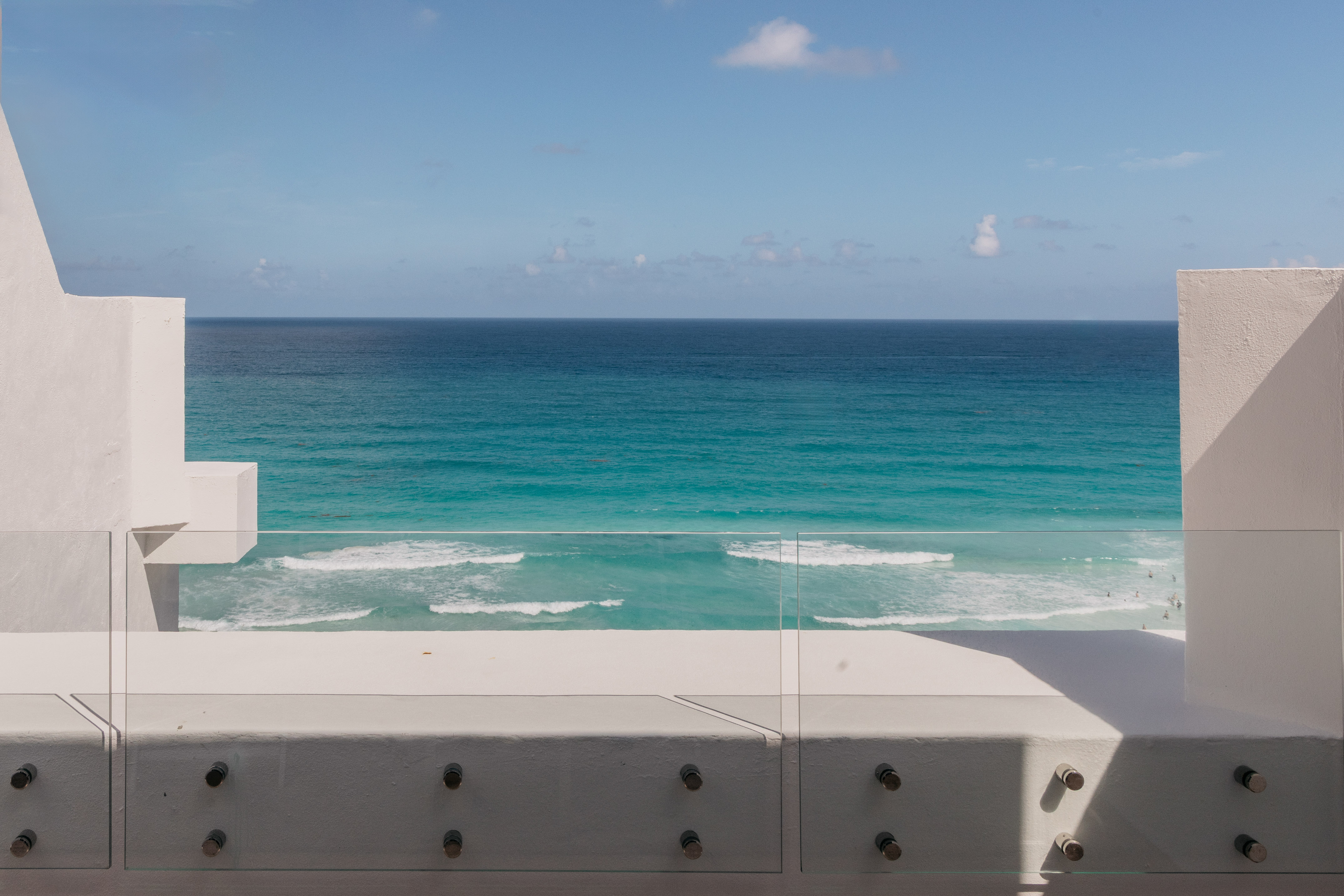 Modern balcony with glass railing, turquoise ocean view, and blue sky.