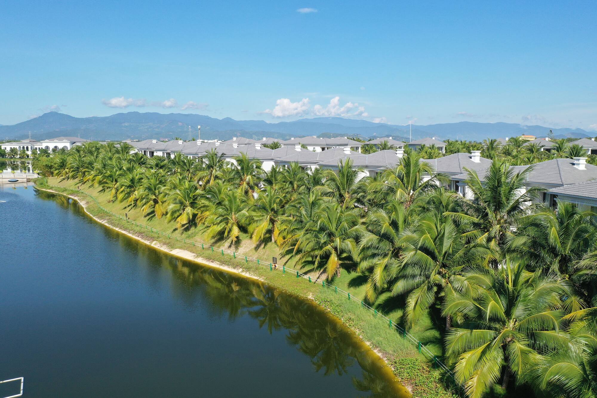 Tropical resort with palm-lined lake, white villas, and distant mountains.