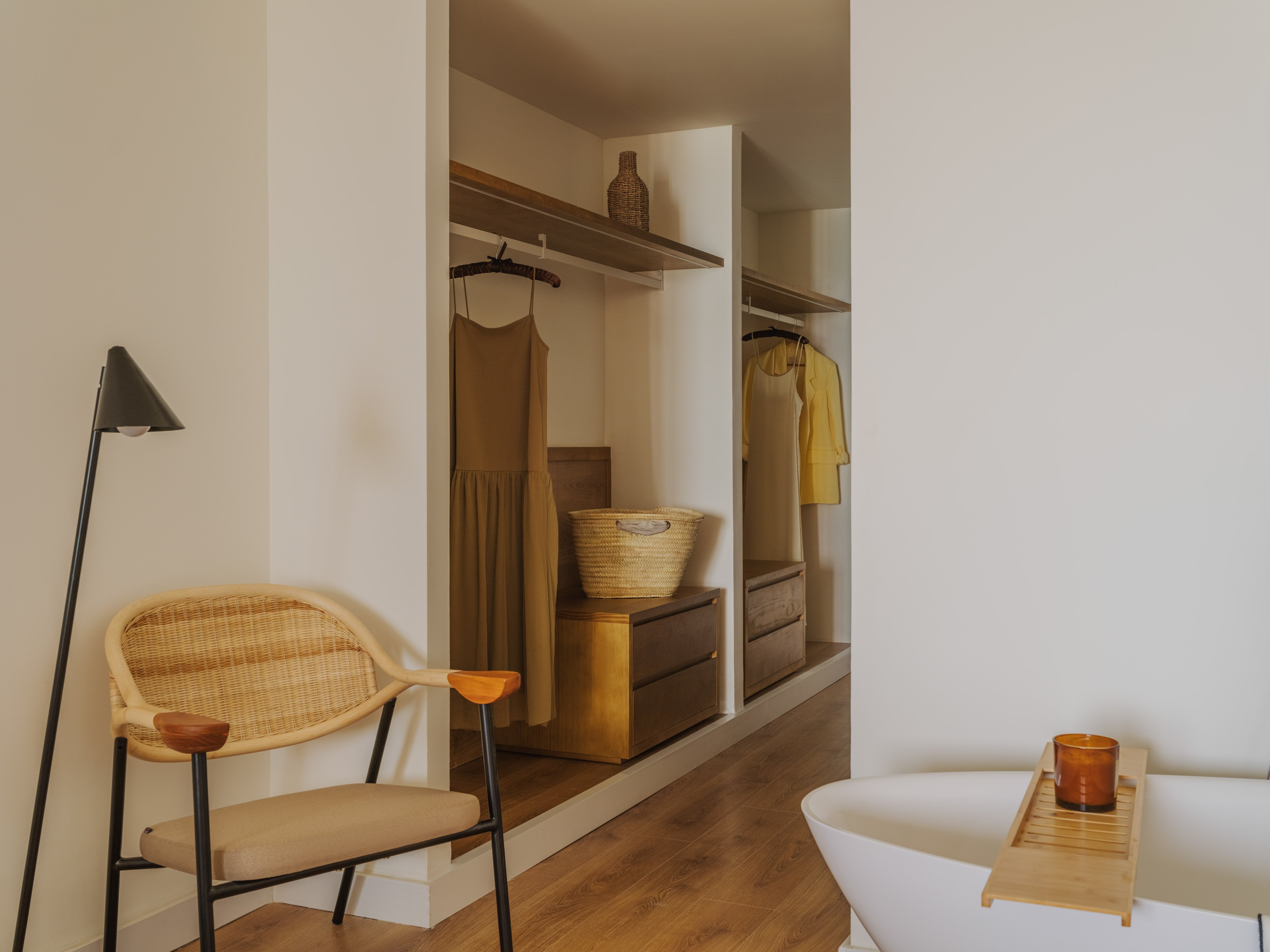 Modern dressing room with open wardrobe, rattan chair, and freestanding bathtub.