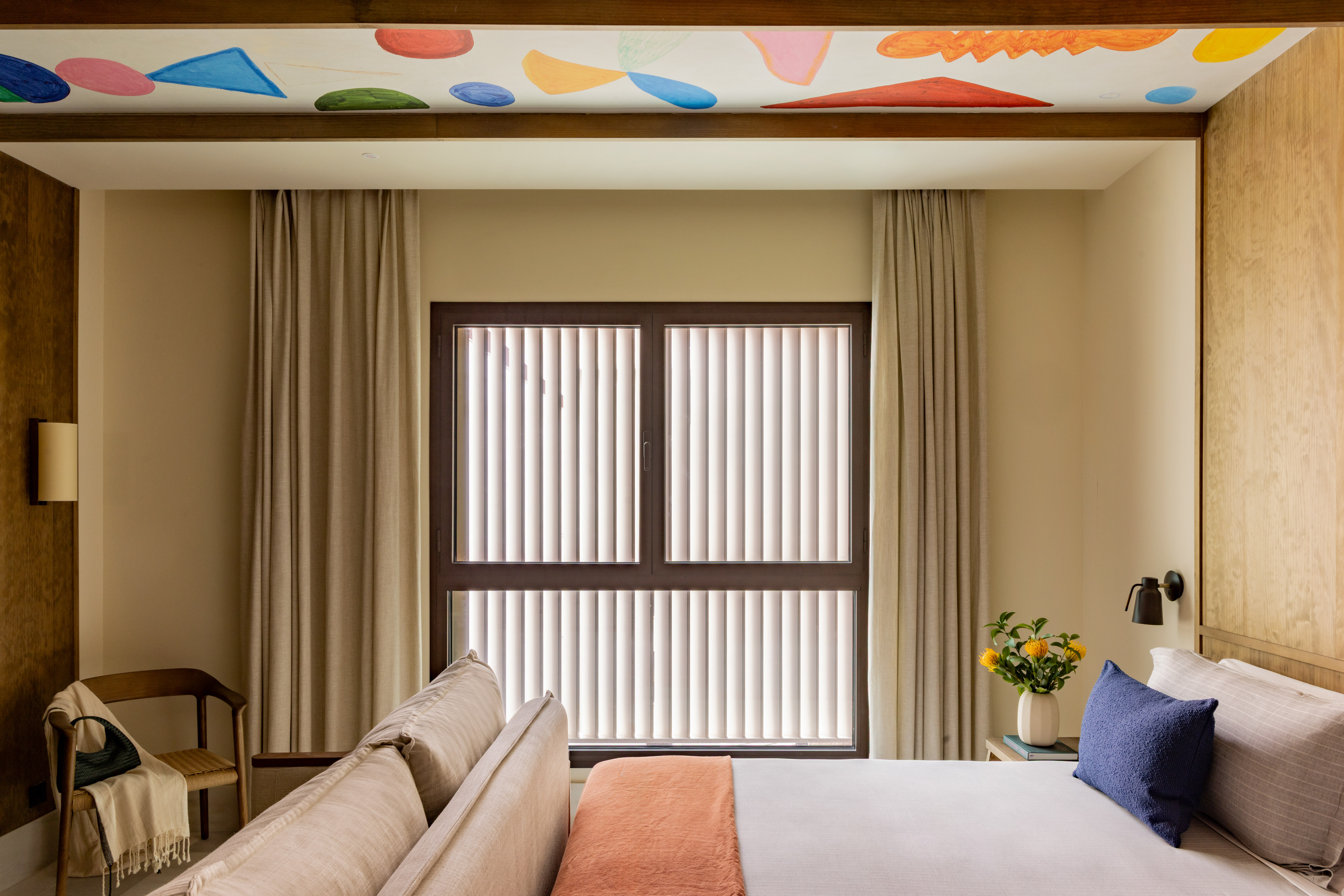 Modern bedroom with colorful abstract ceiling art, window blinds, and cozy bed.