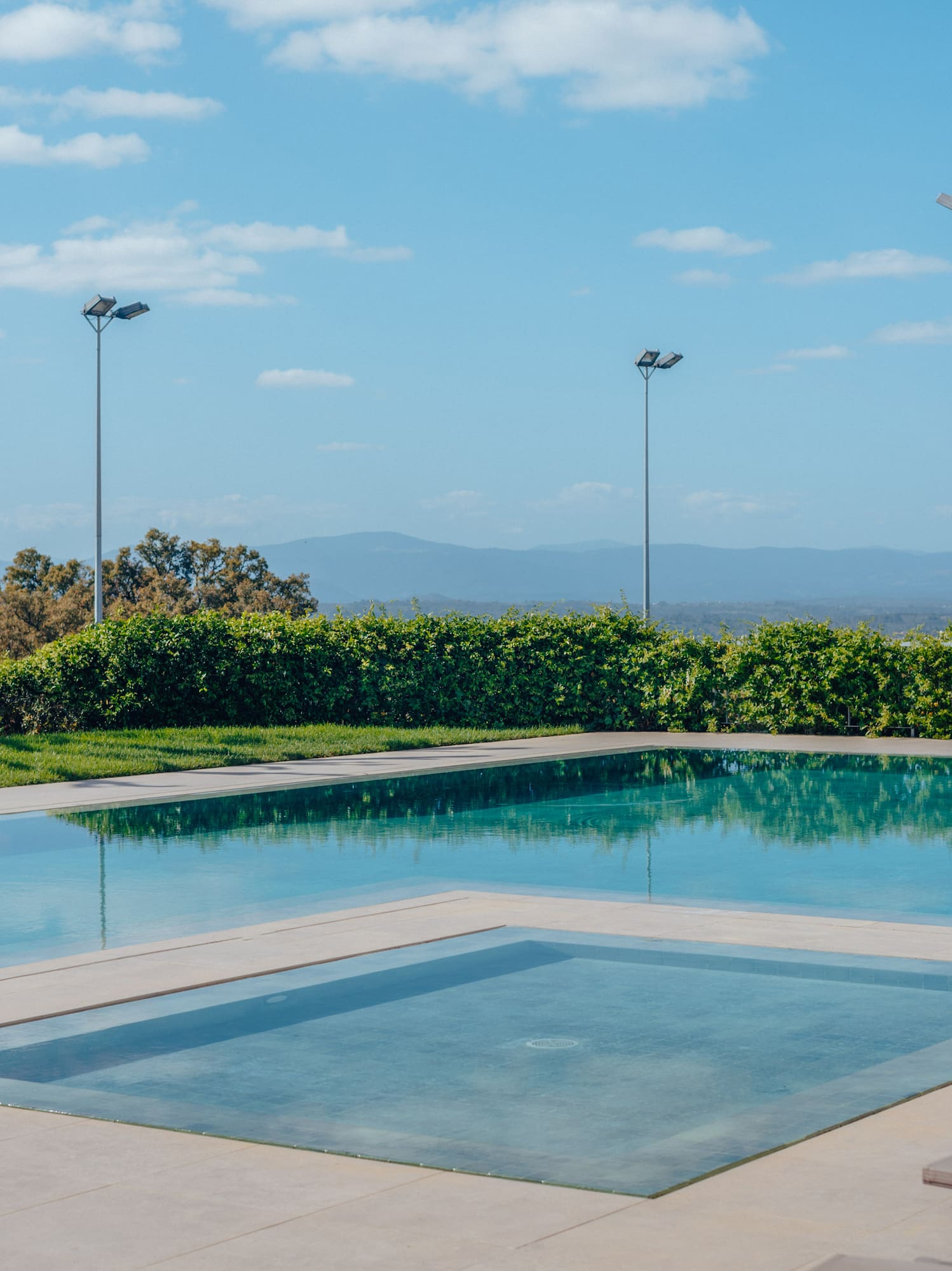 Outdoor swimming pool with integrated spa, mountain views, and sunny blue sky.