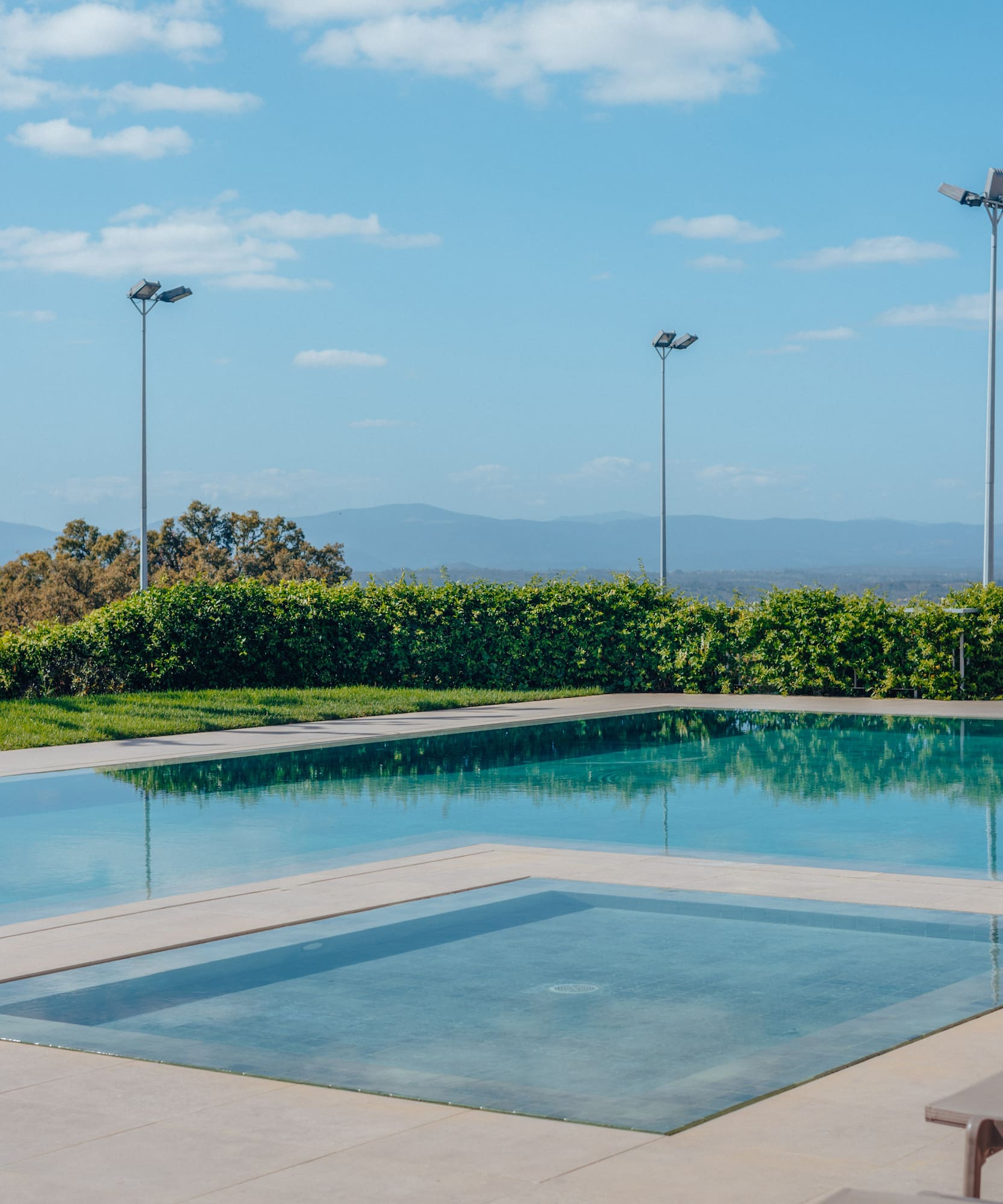 Outdoor swimming pool with integrated spa, mountain views, and sunny blue sky.