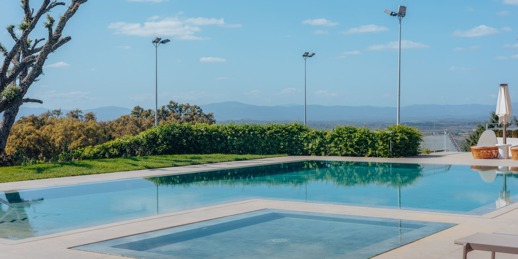 Sunny infinity pool, plunge pool, and patio overlooking a mountain landscape.