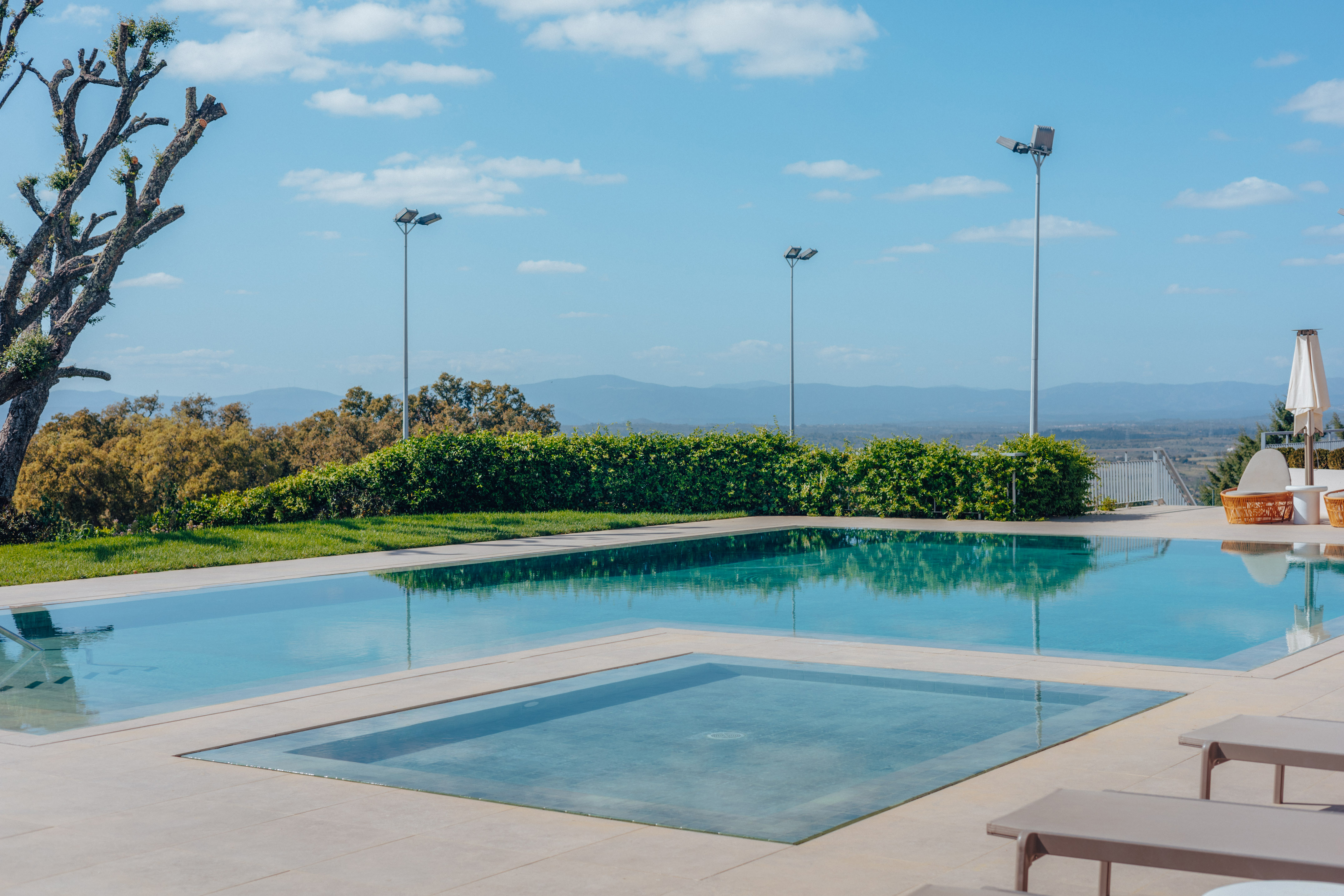 Sunny infinity pool, plunge pool, and patio overlooking a mountain landscape.