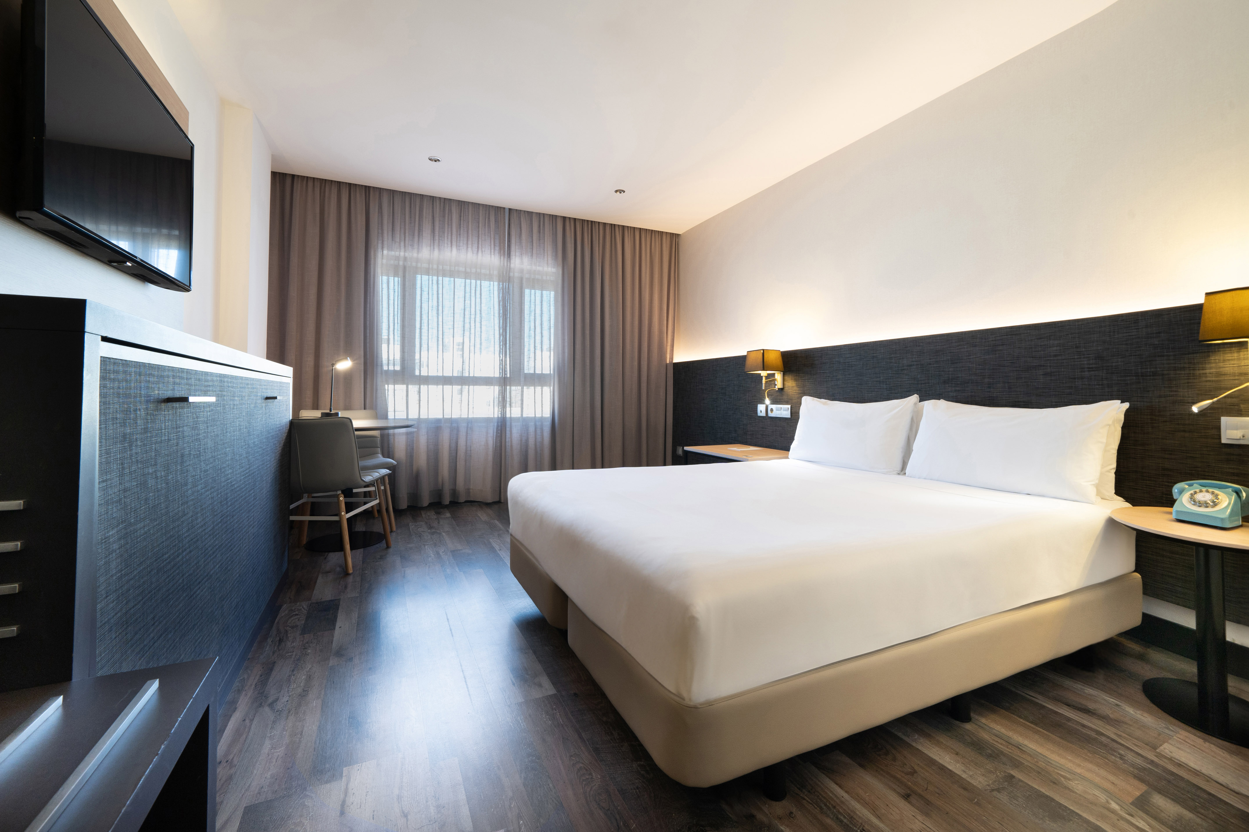 Spacious modern hotel room with king bed, wood floors, work desk, and large window.