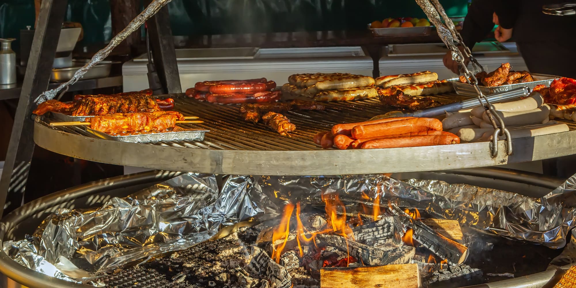 Bratwurst, sausages, and ribs grilling on a large BBQ over hot coals.