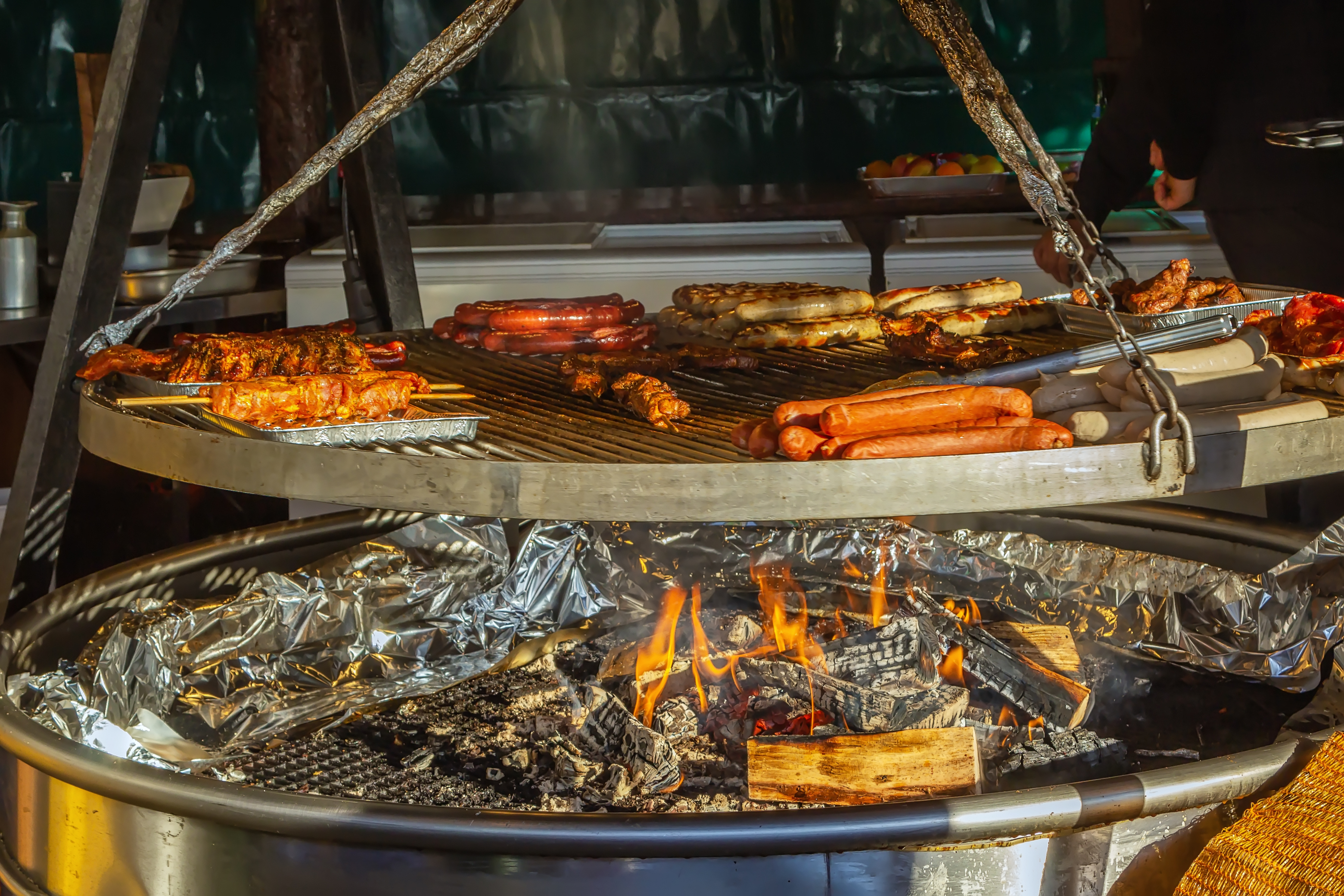 Bratwurst, sausages, and ribs grilling on a large BBQ over hot coals.
