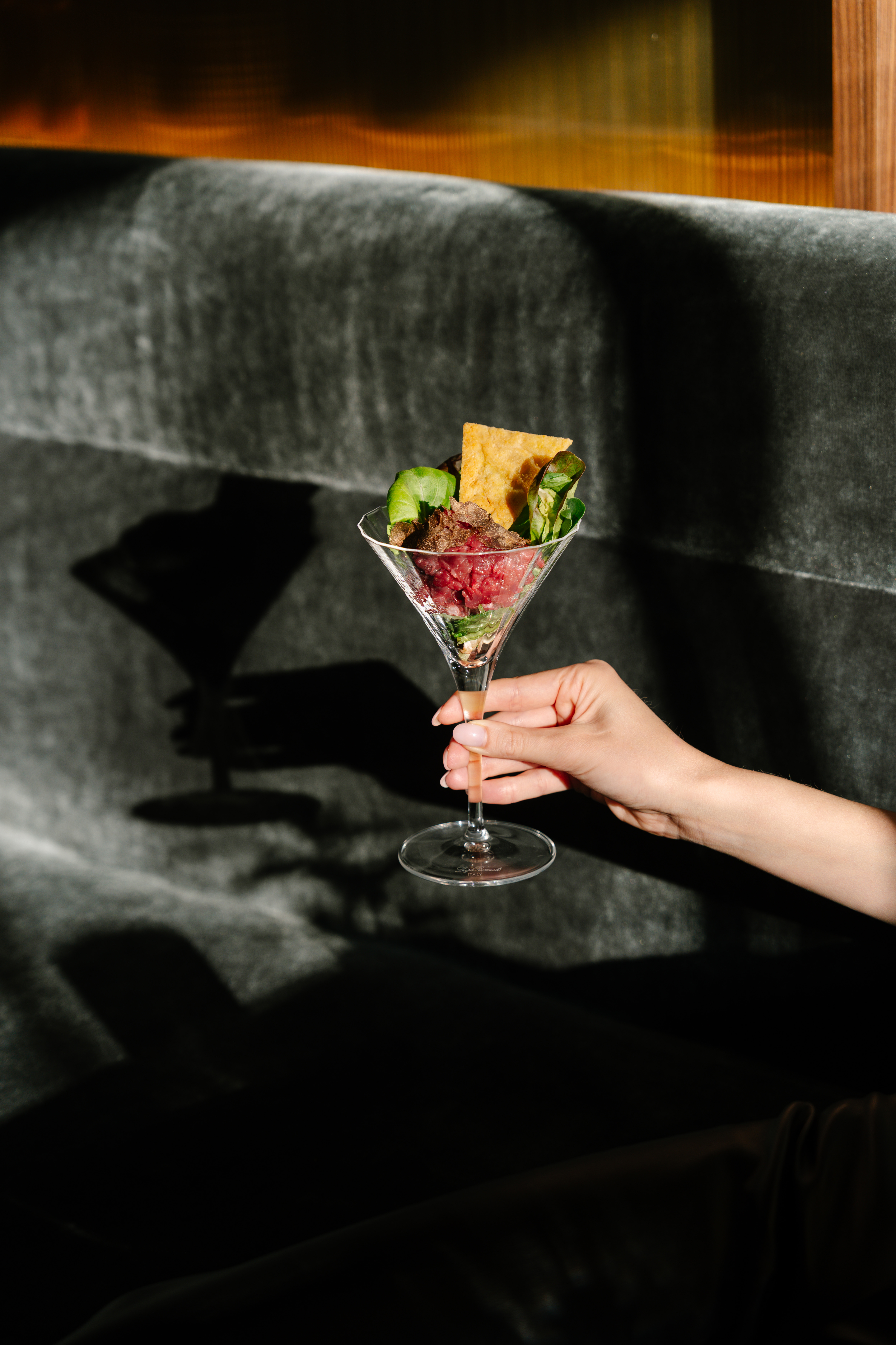 Martini glass with beef tartare, greens, and crispy chip, held by hand.
