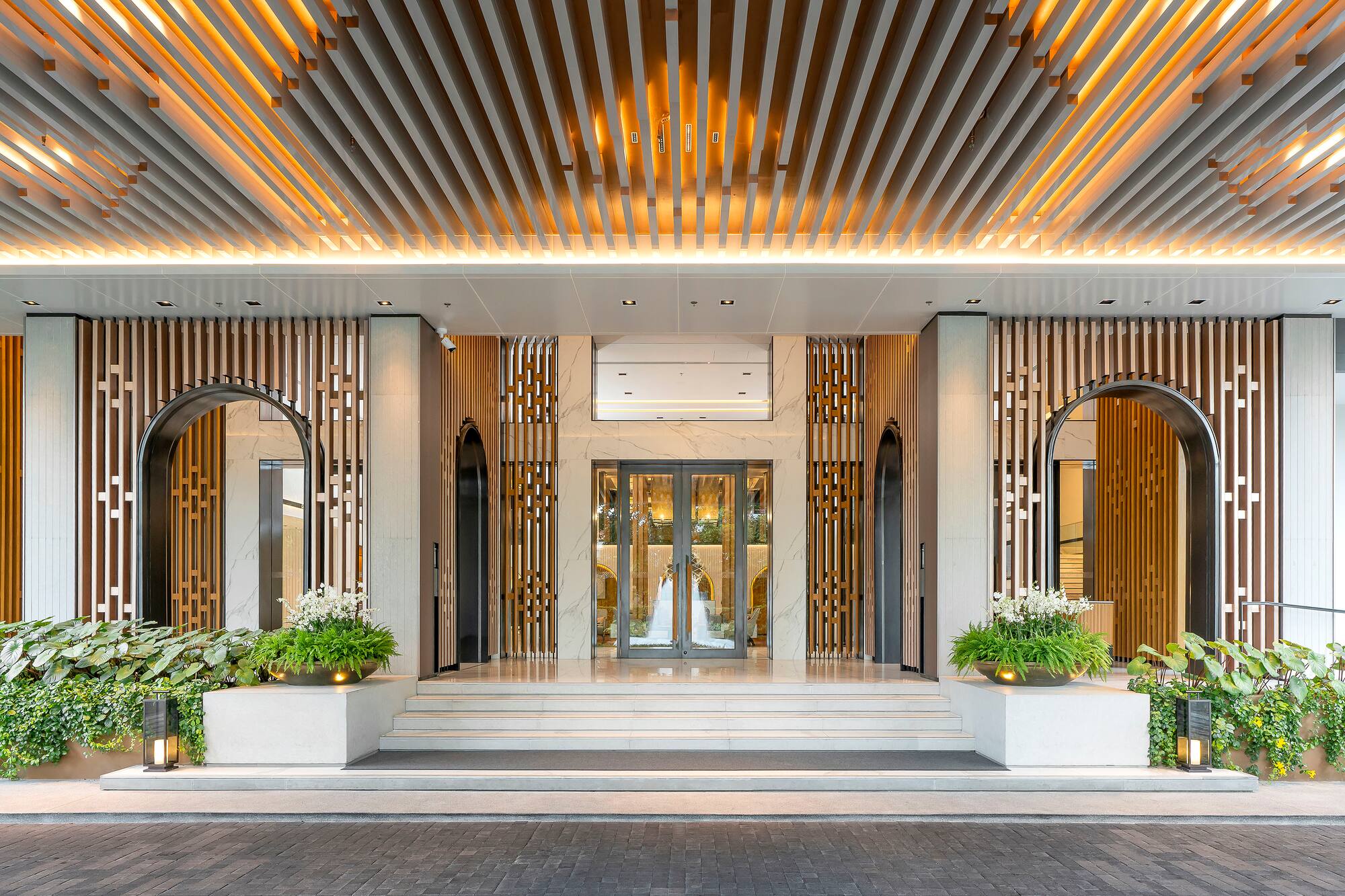 Luxurious hotel entrance featuring illuminated wood ceiling and marble facade.