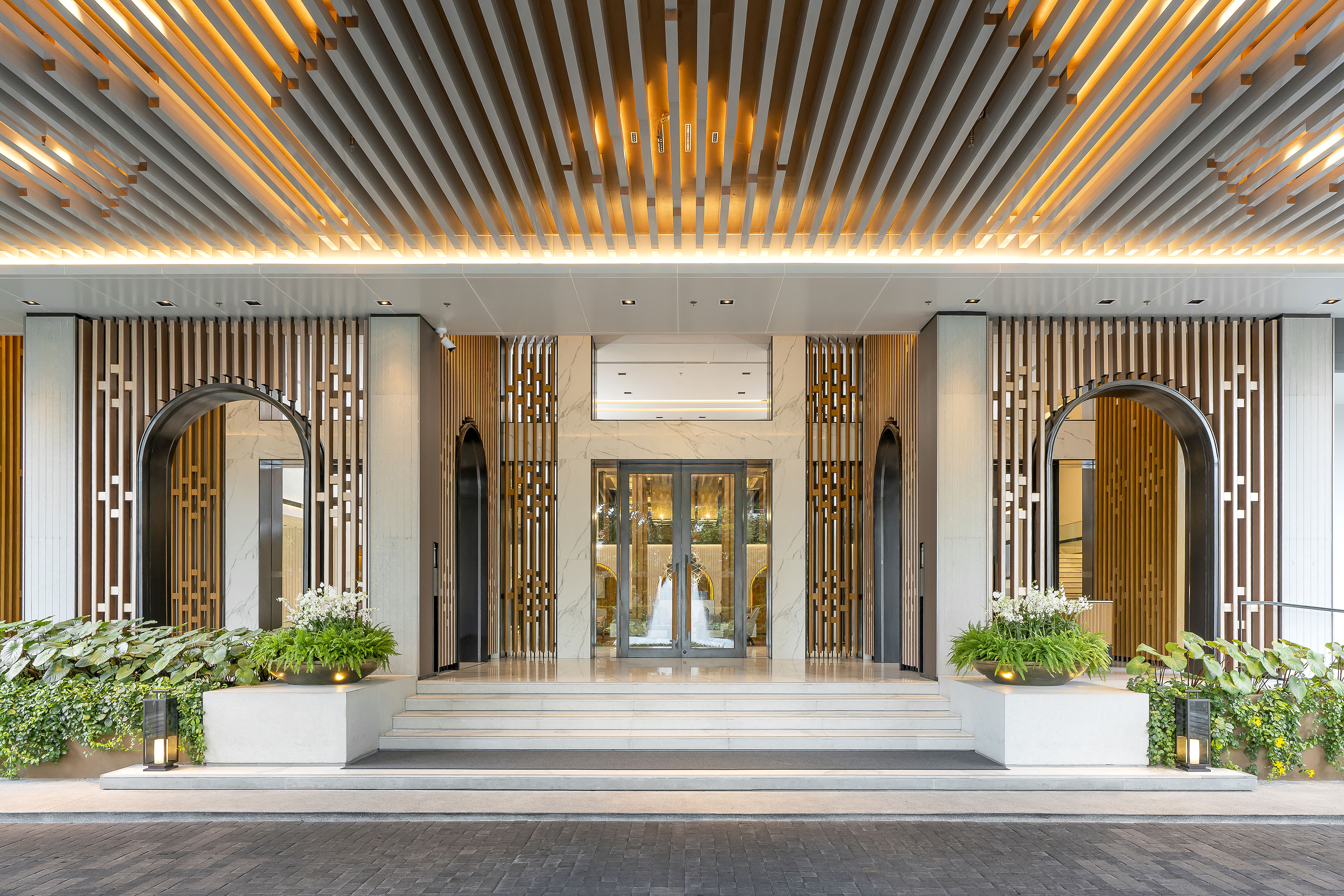 Luxurious hotel entrance featuring illuminated wood ceiling and marble facade.