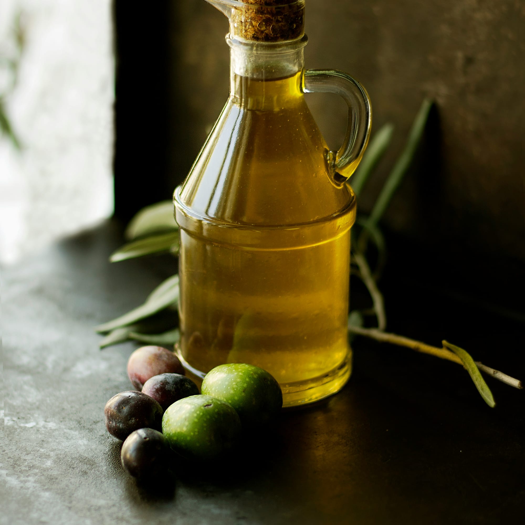 Extra virgin olive oil in glass bottle with fresh green and black olives.