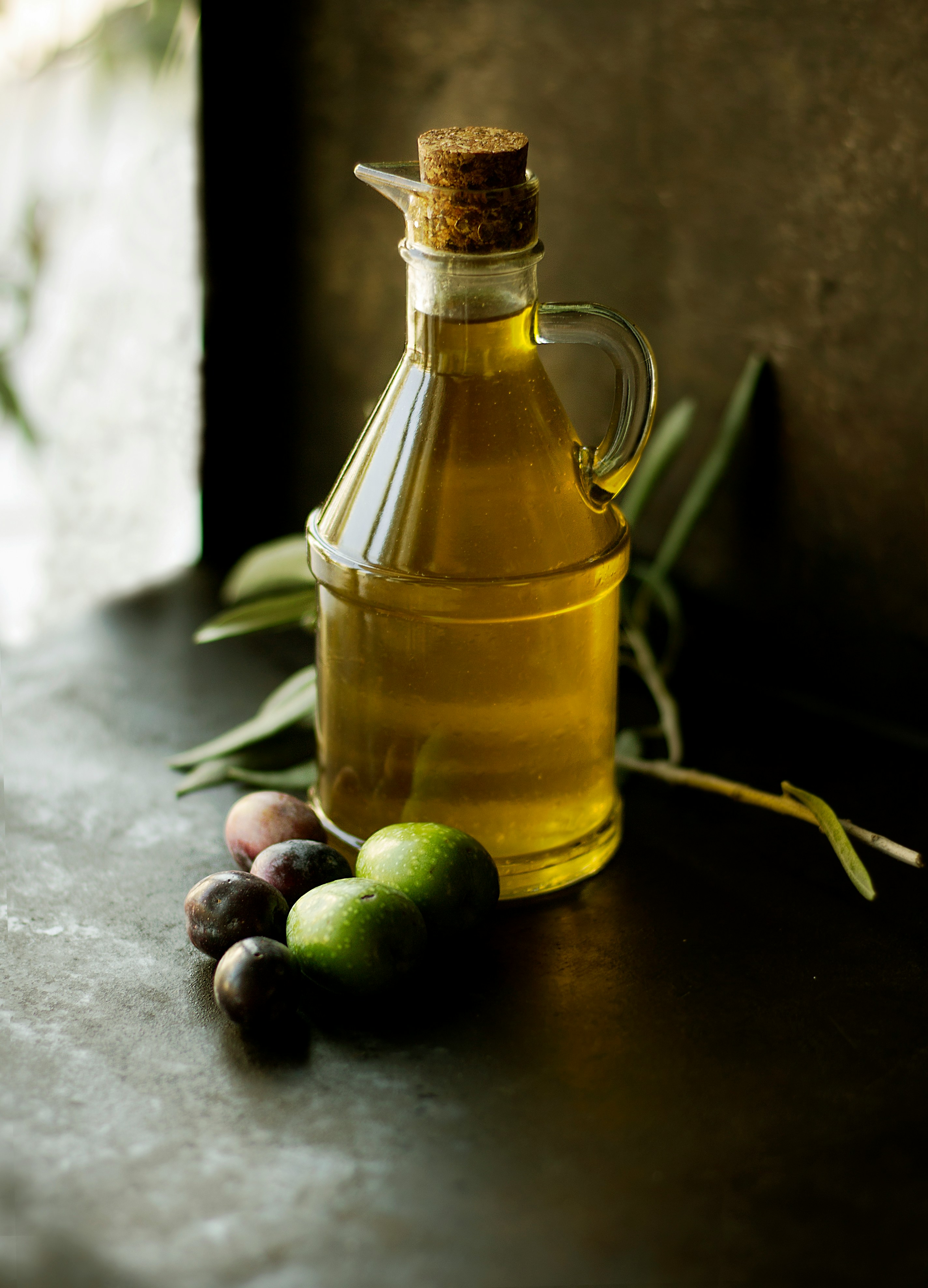 Extra virgin olive oil in glass bottle with fresh green and black olives.