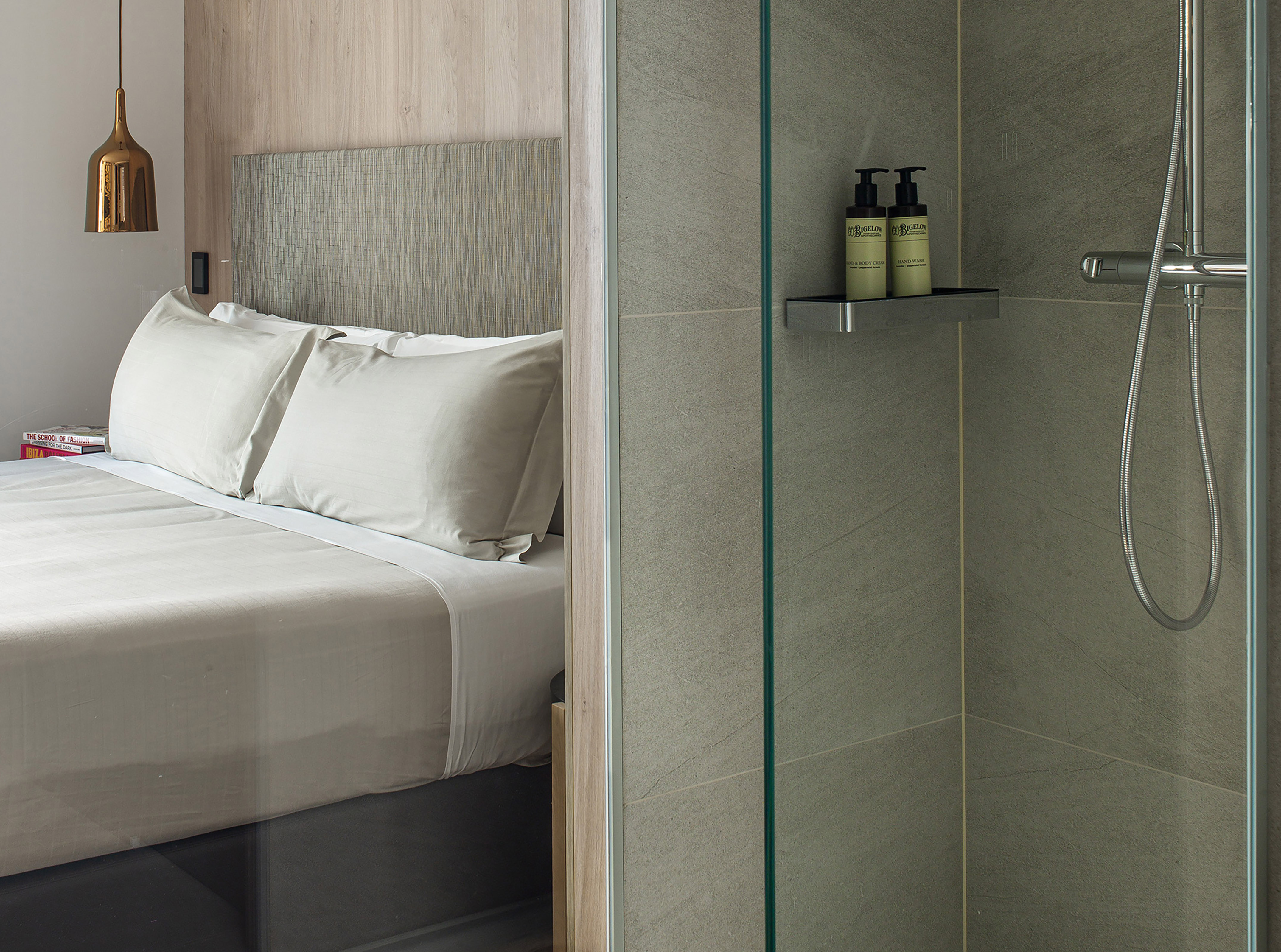 Modern hotel room with bed, pendant light, and ensuite glass shower.