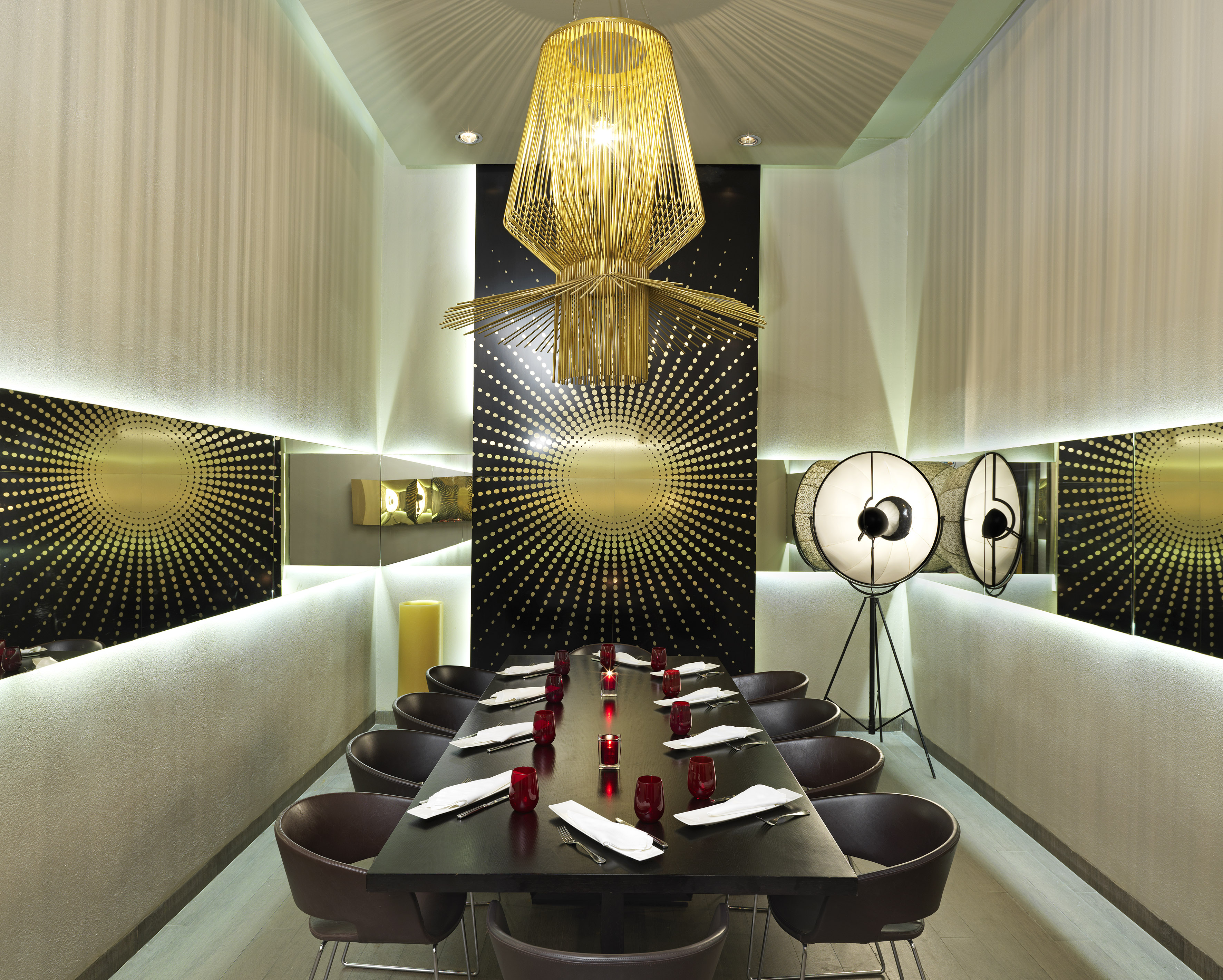 Modern private dining room with long table, golden chandelier, sunburst wall.