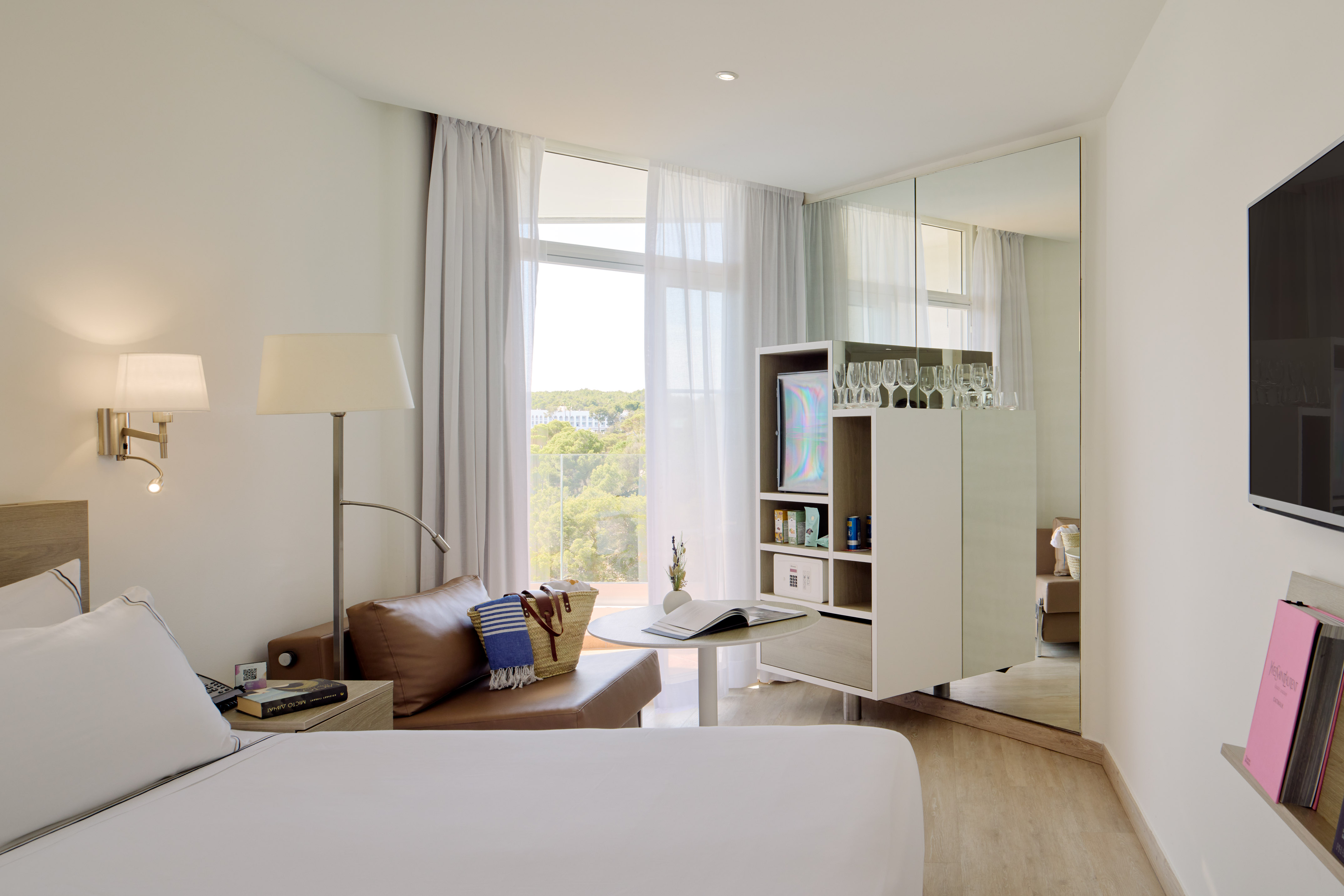 Bright hotel bedroom with white bed, window to balcony, and sleek amenities.