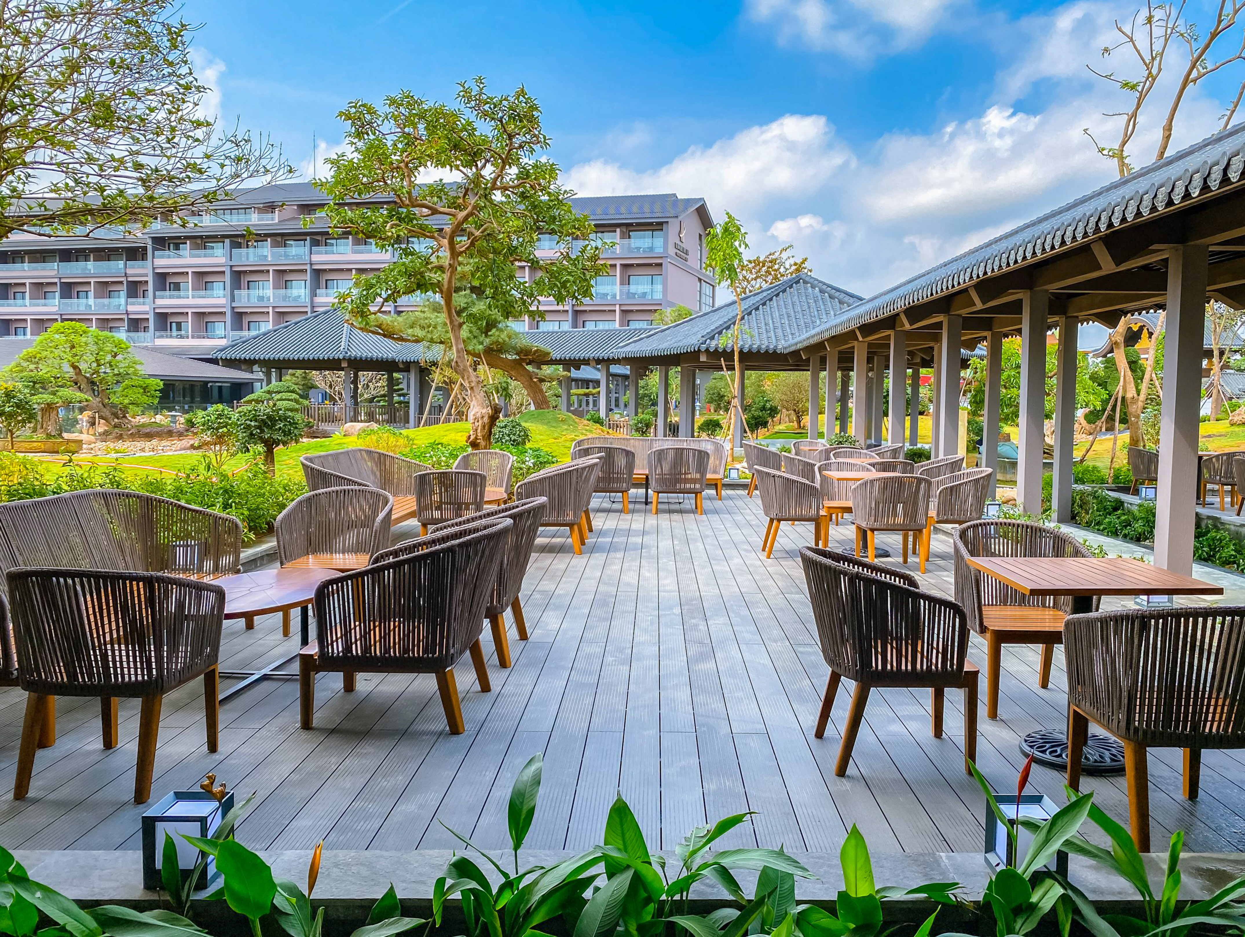 Outdoor dining patio with wicker seating, hotel backdrop, and Asian-style garden.