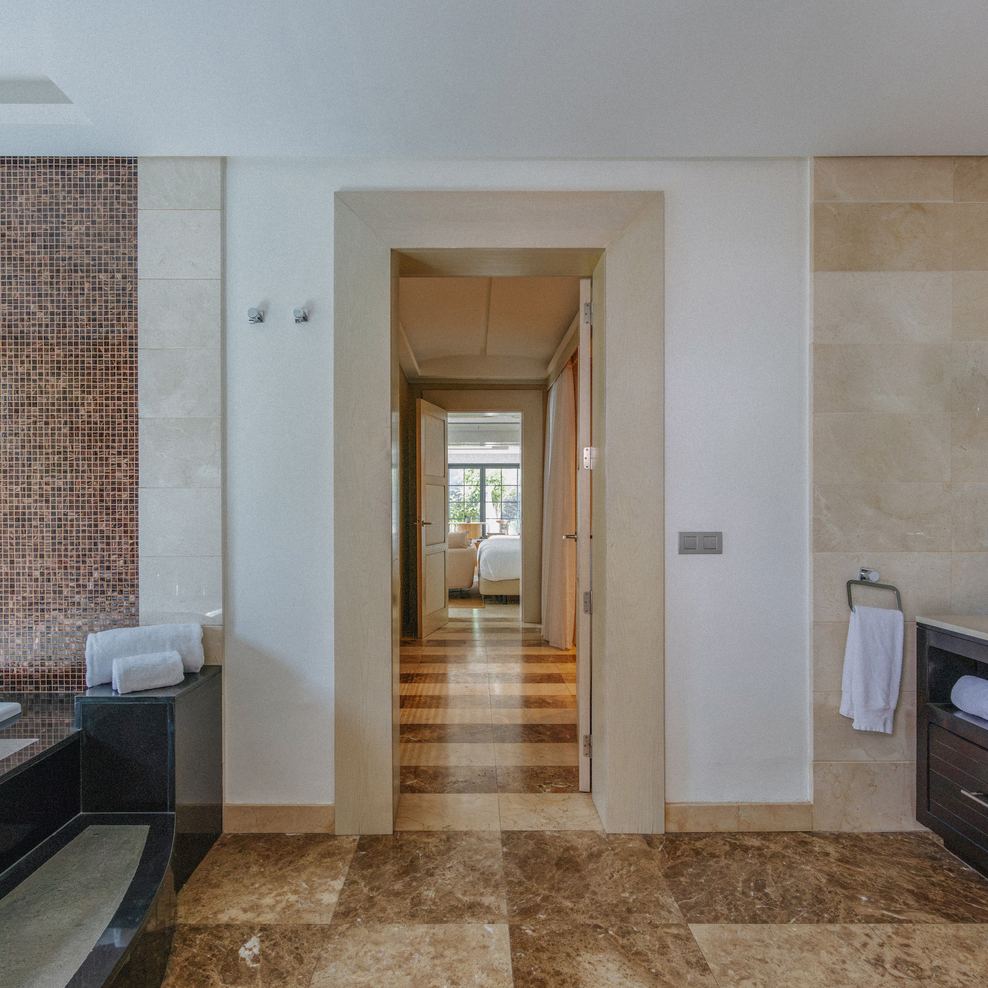 Luxury bathroom with mosaic wall, marble floor, tub, vanity, and bedroom view.