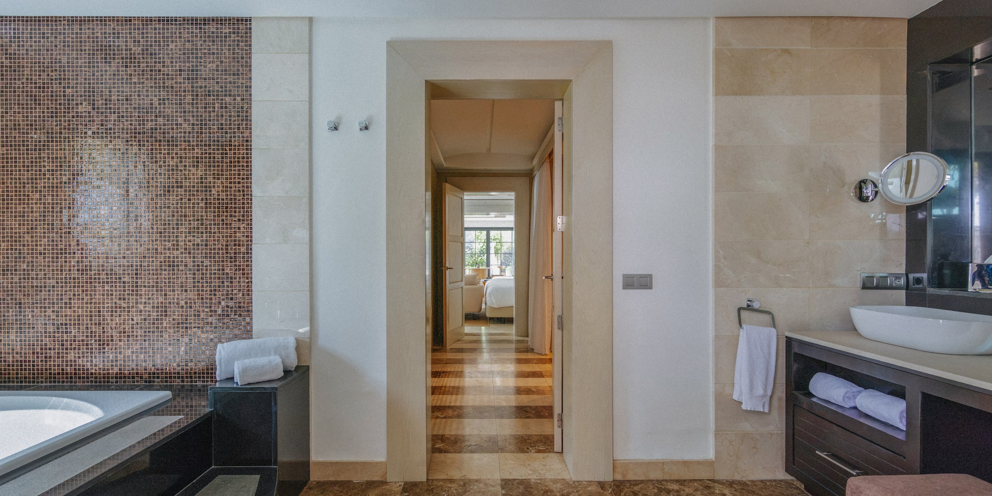 Luxury bathroom with mosaic wall, marble floor, vanity, and bedroom view.