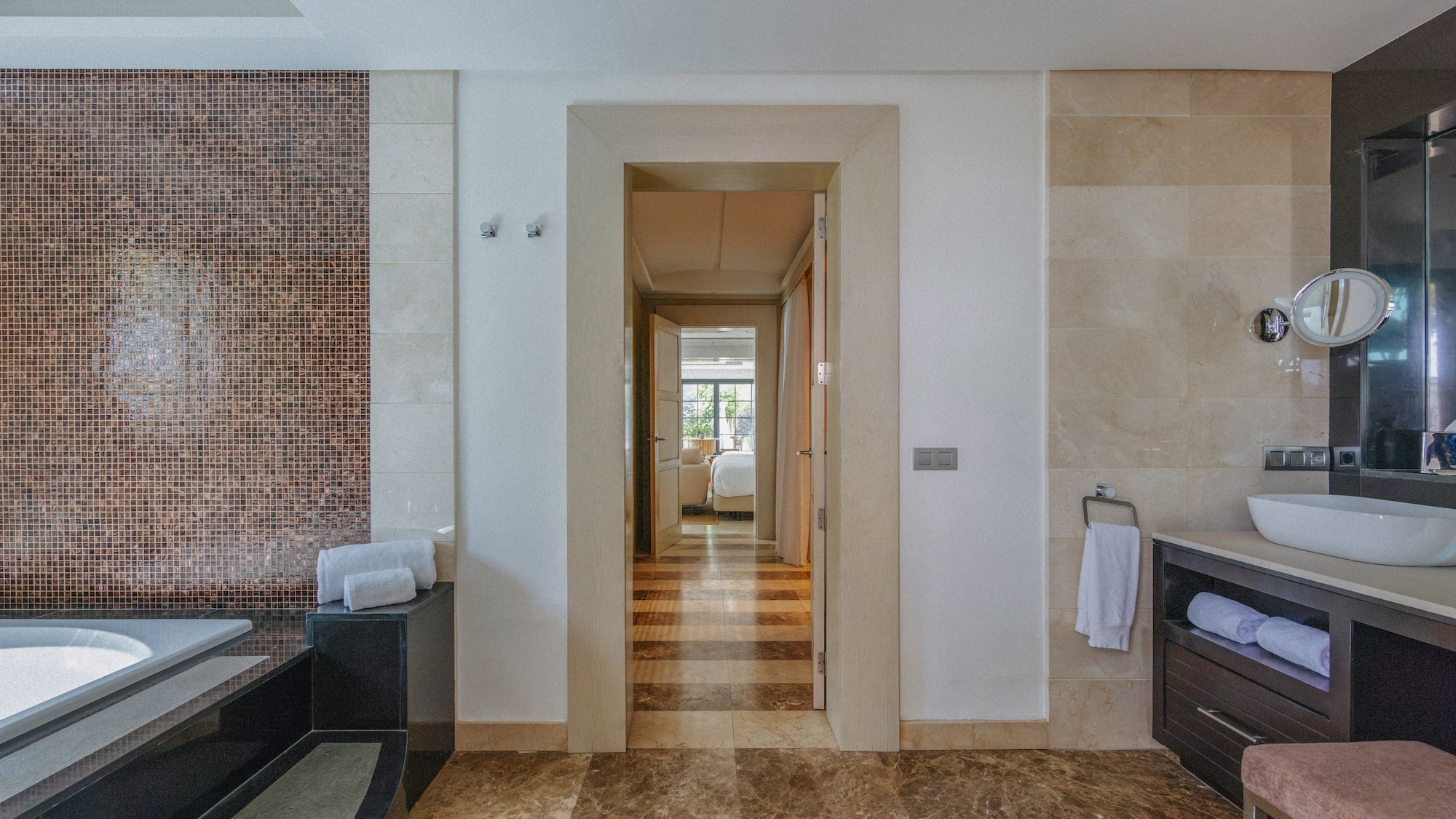 Luxury bathroom with mosaic wall, marble floor, vanity, and bedroom view.