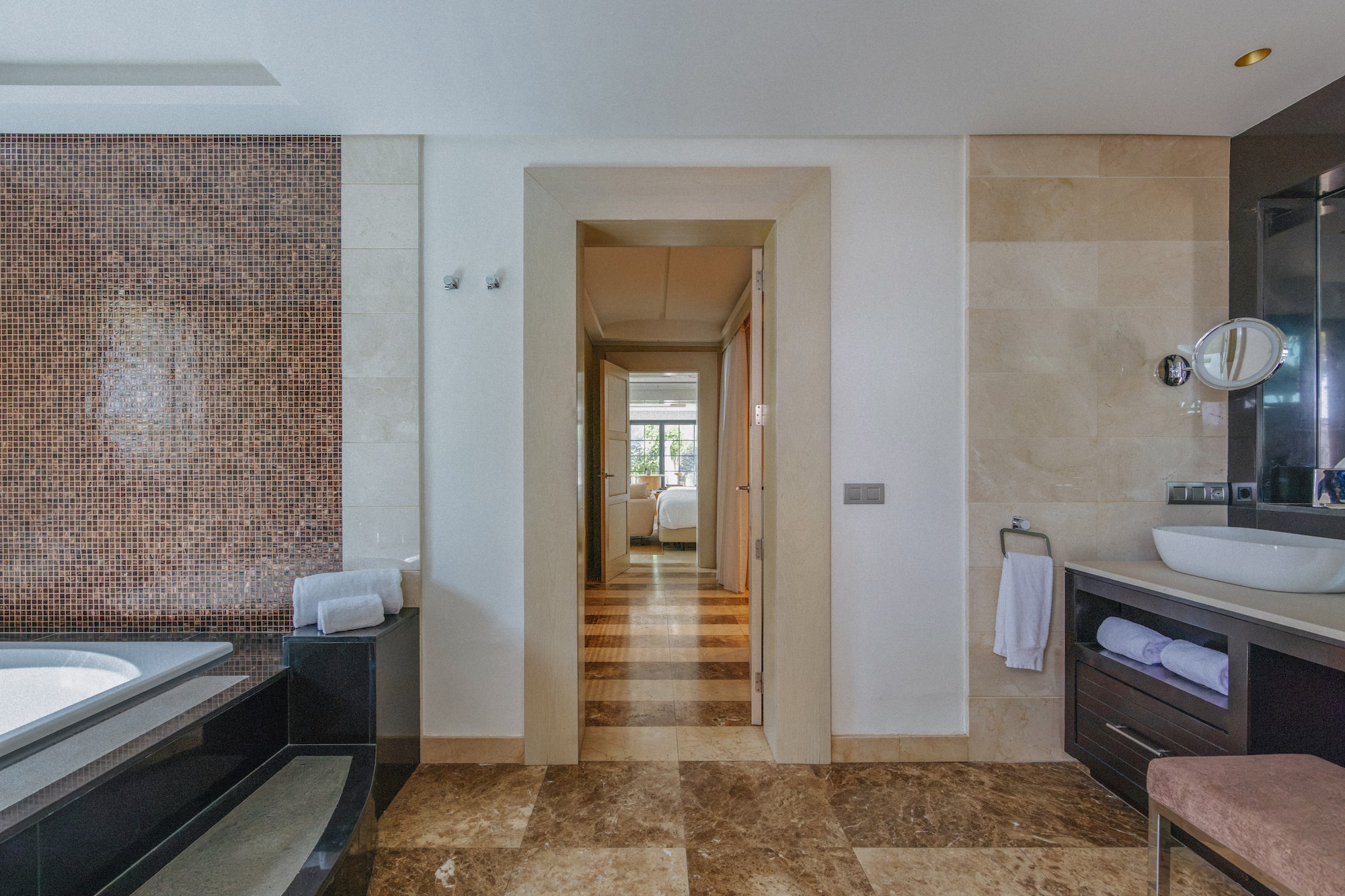Luxury bathroom with mosaic wall, marble floor, vanity, and bedroom view.