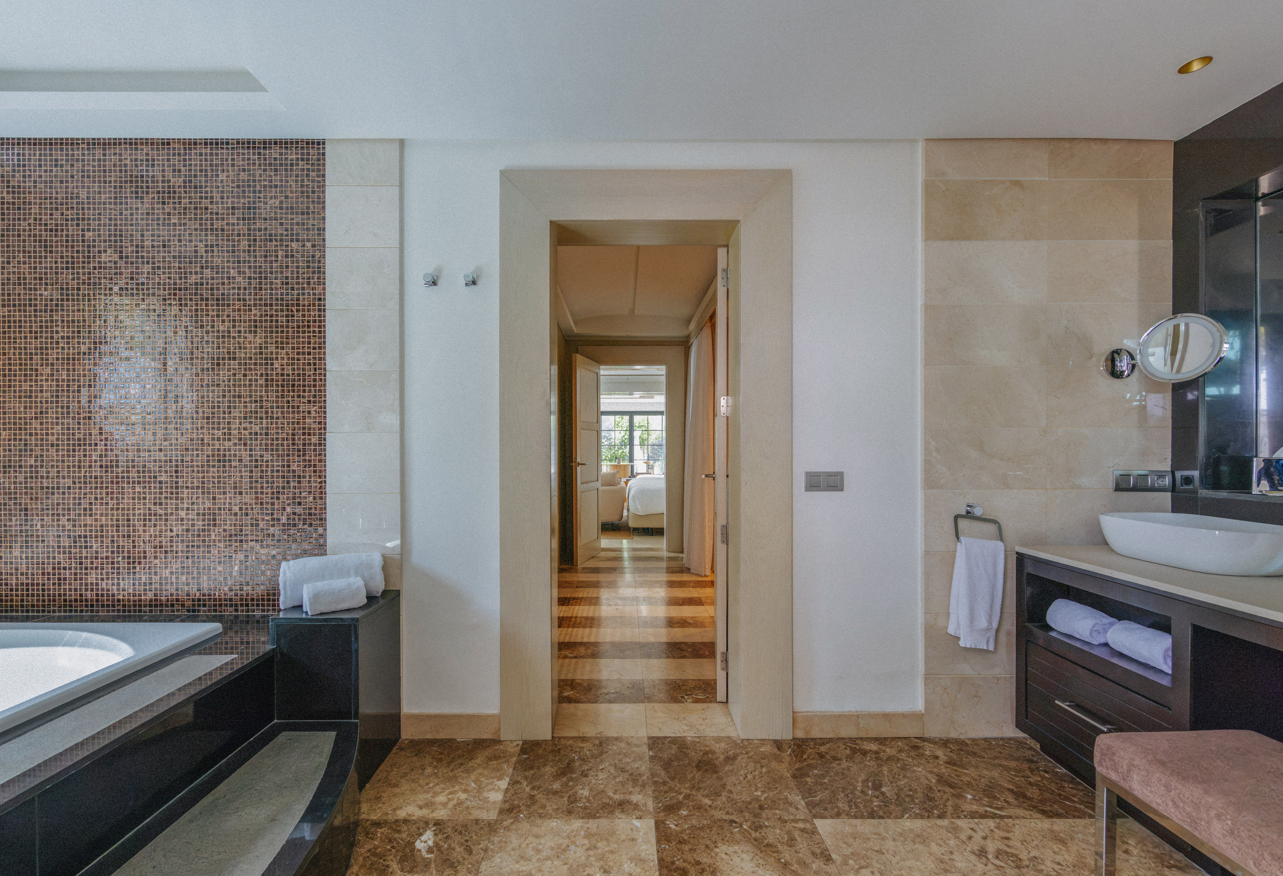 Luxury bathroom with mosaic wall, marble floor, vanity, and bedroom view.