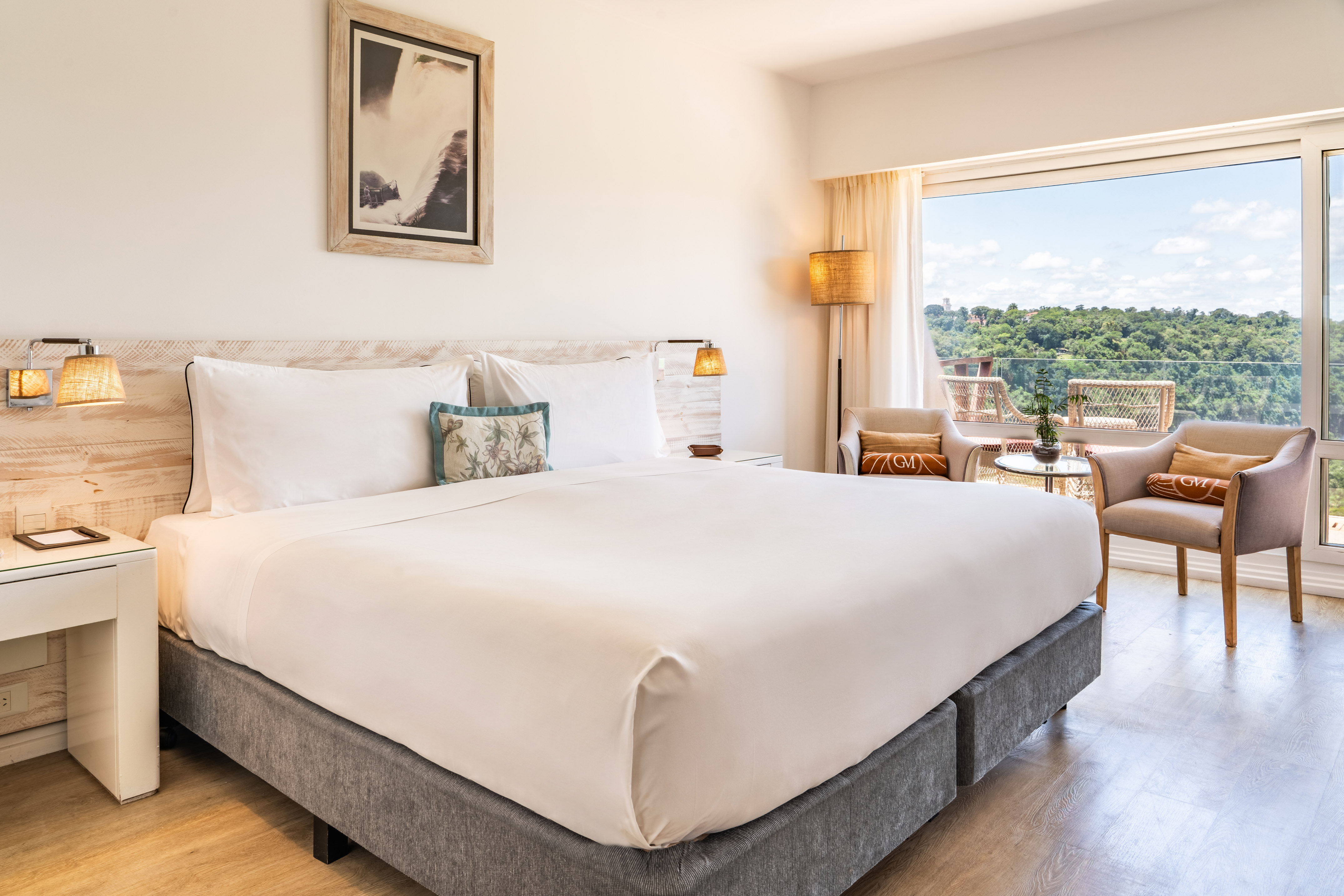 Bright hotel room with large bed, balcony, and lush forest view.