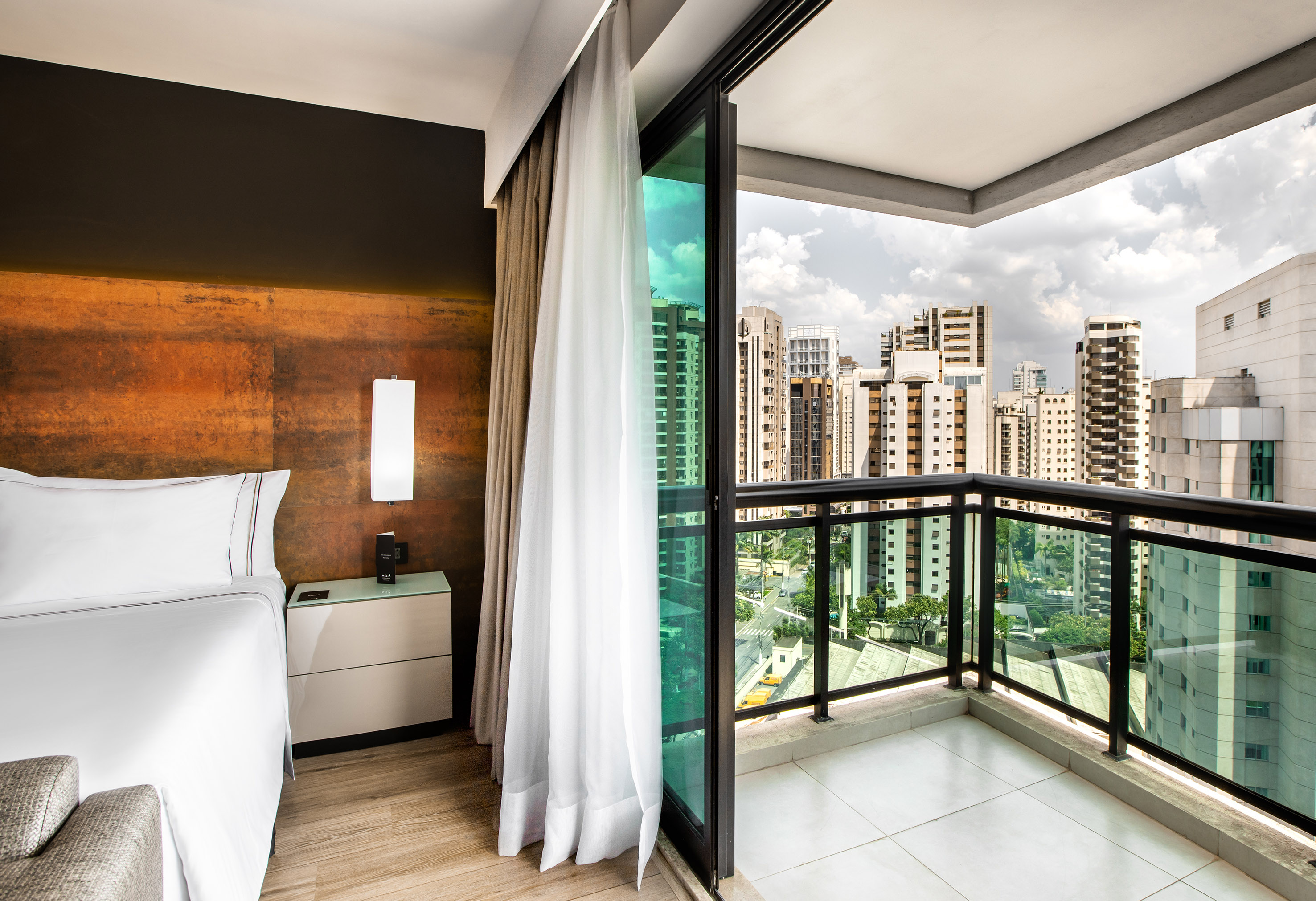 Hotel room with bed, private balcony, and urban city skyline view.