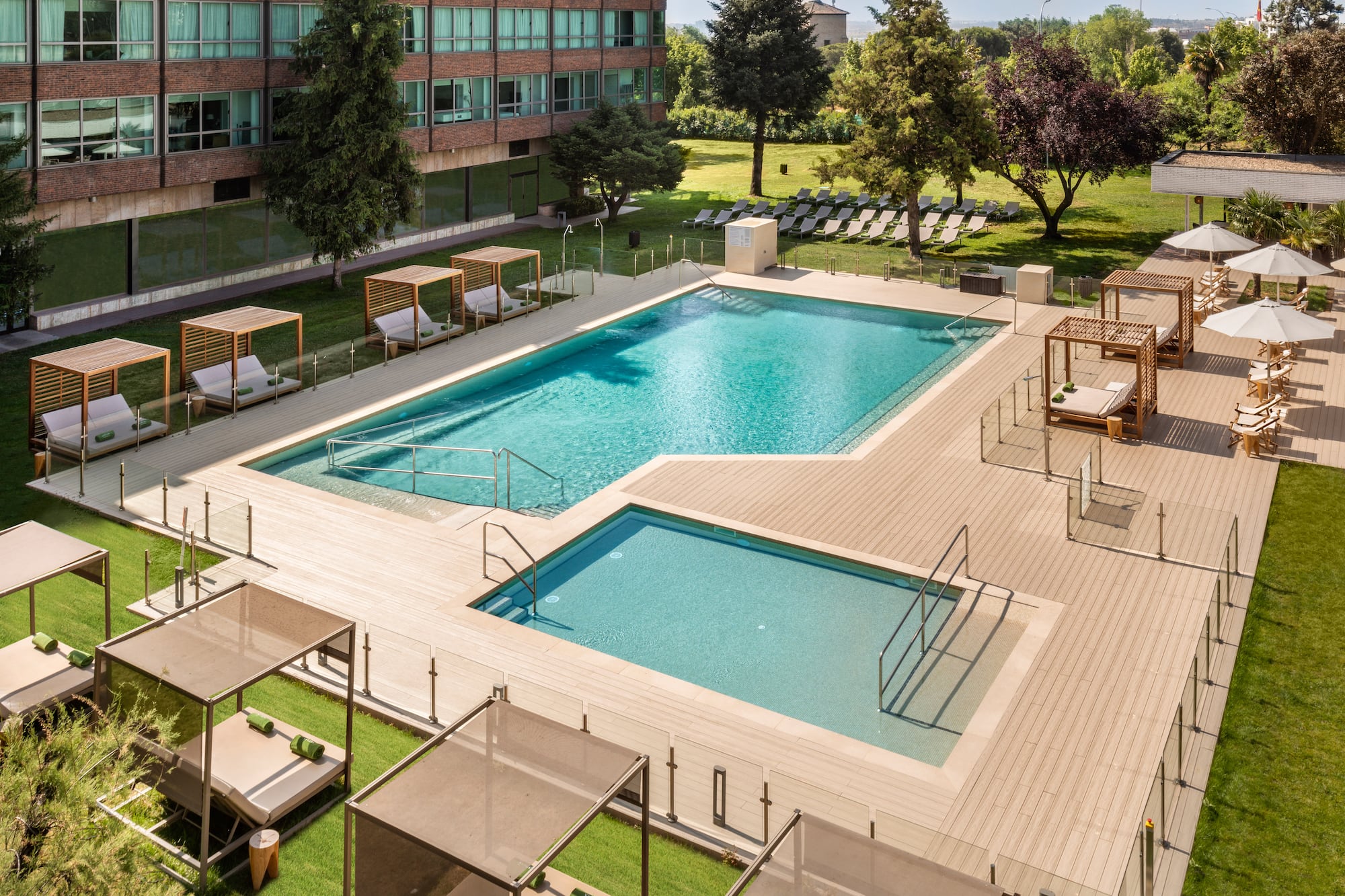 Hotel outdoor pool area with two pools, wooden deck, sunbeds, and green grass.