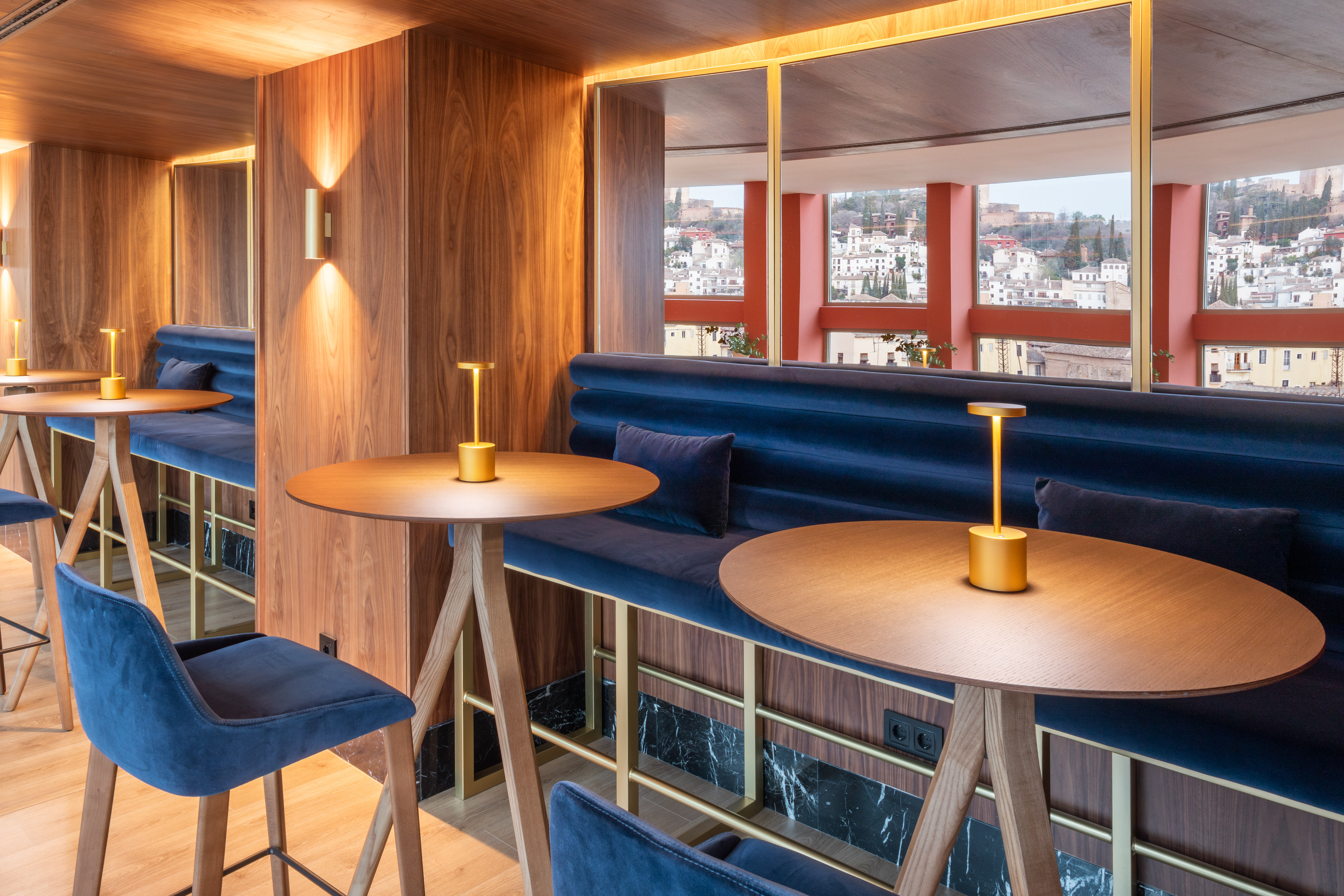 Modern bar interior with wood walls, navy velvet seating, and panoramic city view.