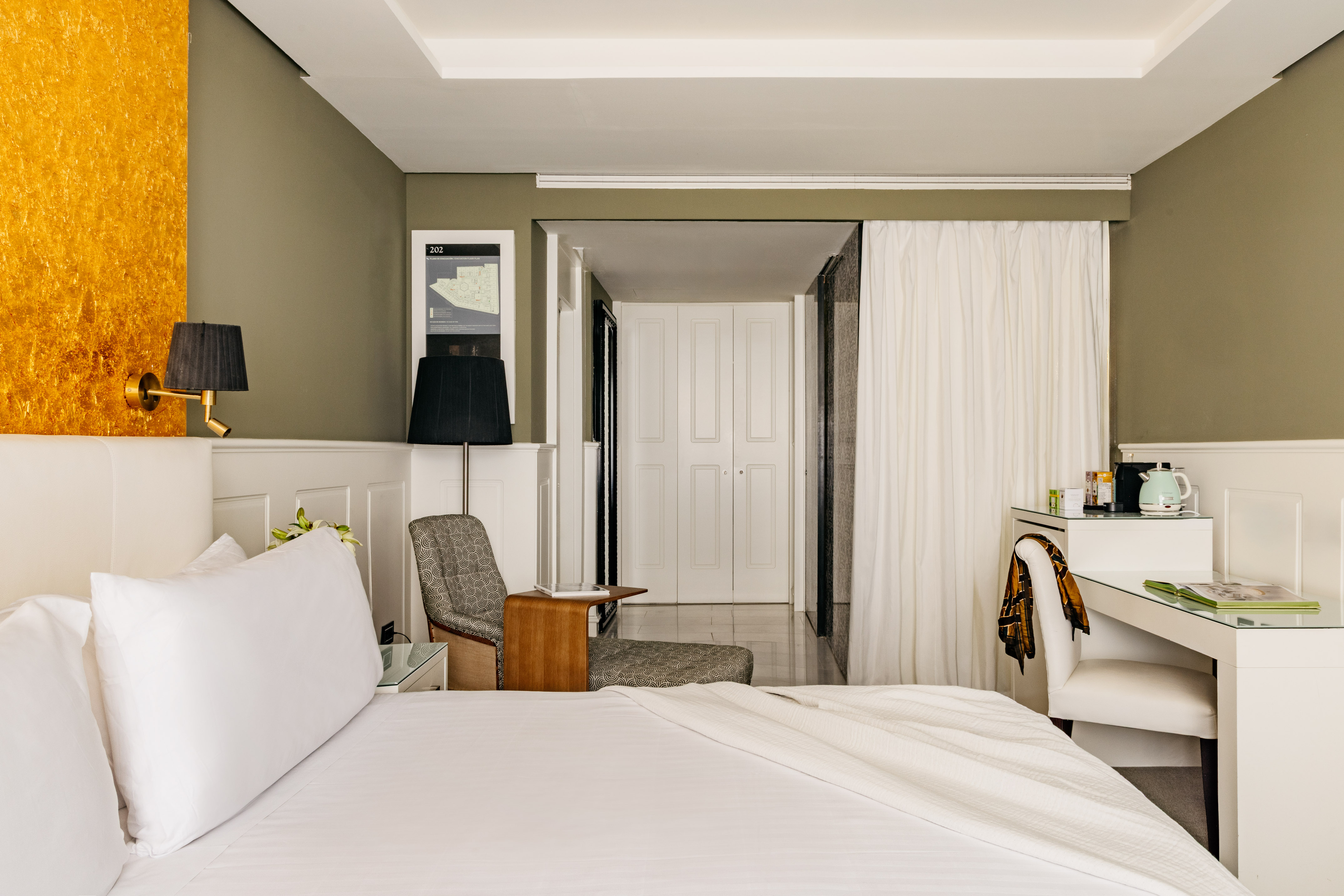 Modern hotel bedroom with white bed, golden accent wall, and work desk.