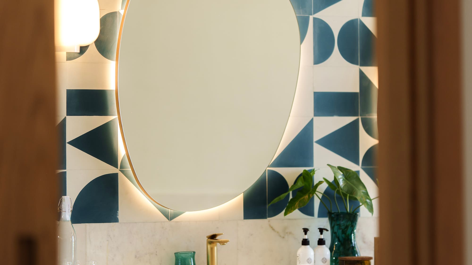 Modern bathroom vanity with backlit mirror, geometric teal tiles, and wood cabinet.