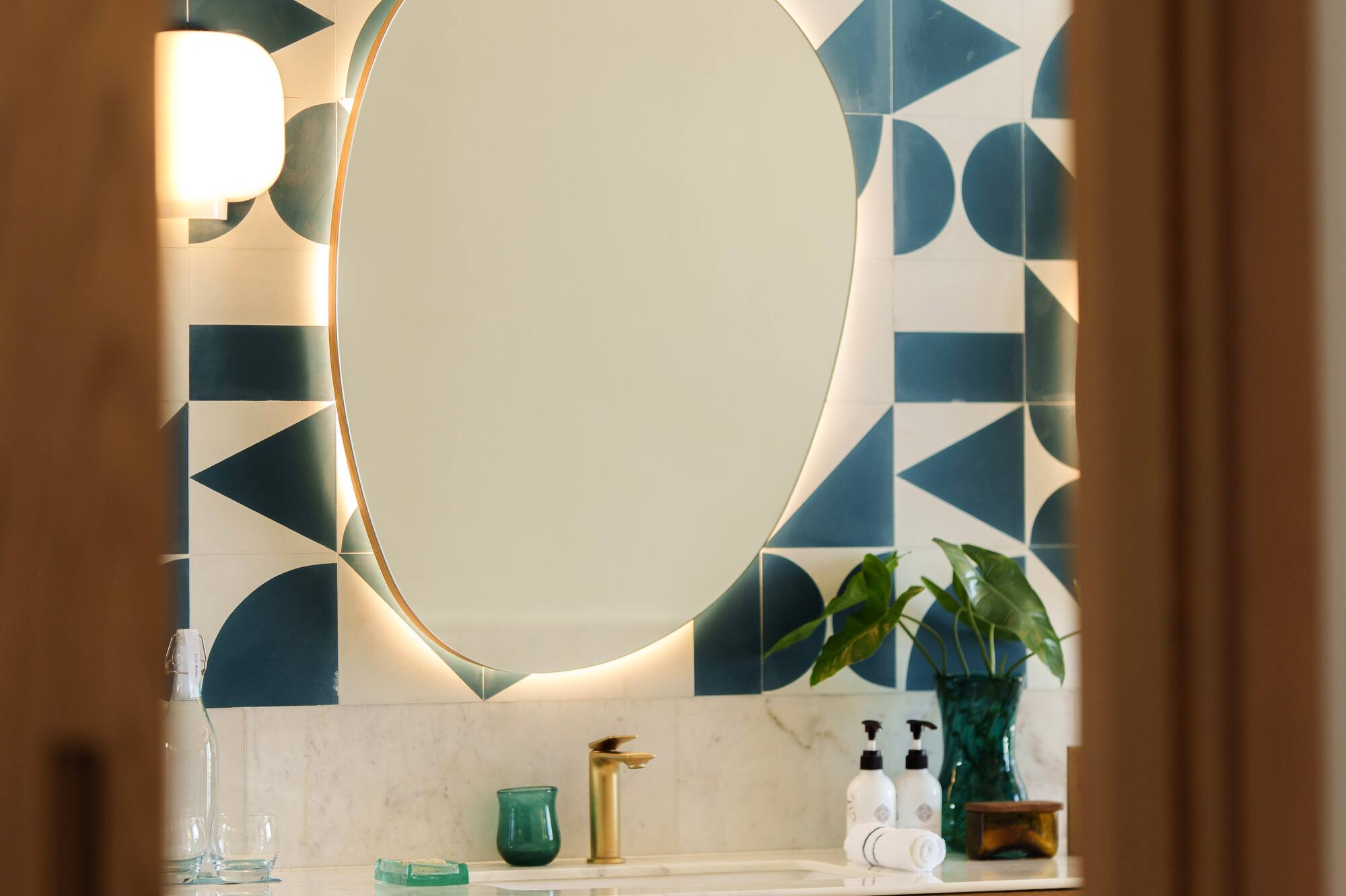 Modern bathroom vanity with backlit mirror, geometric teal tiles, and wood cabinet.