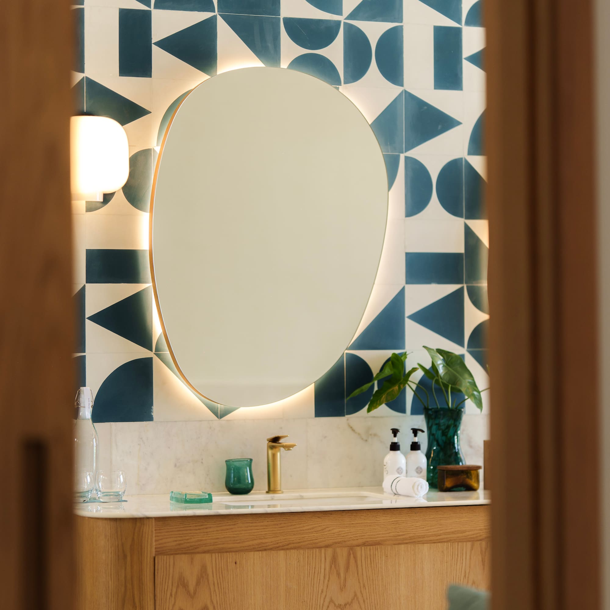 Modern bathroom vanity with backlit mirror, geometric teal tiles, and wood cabinet.