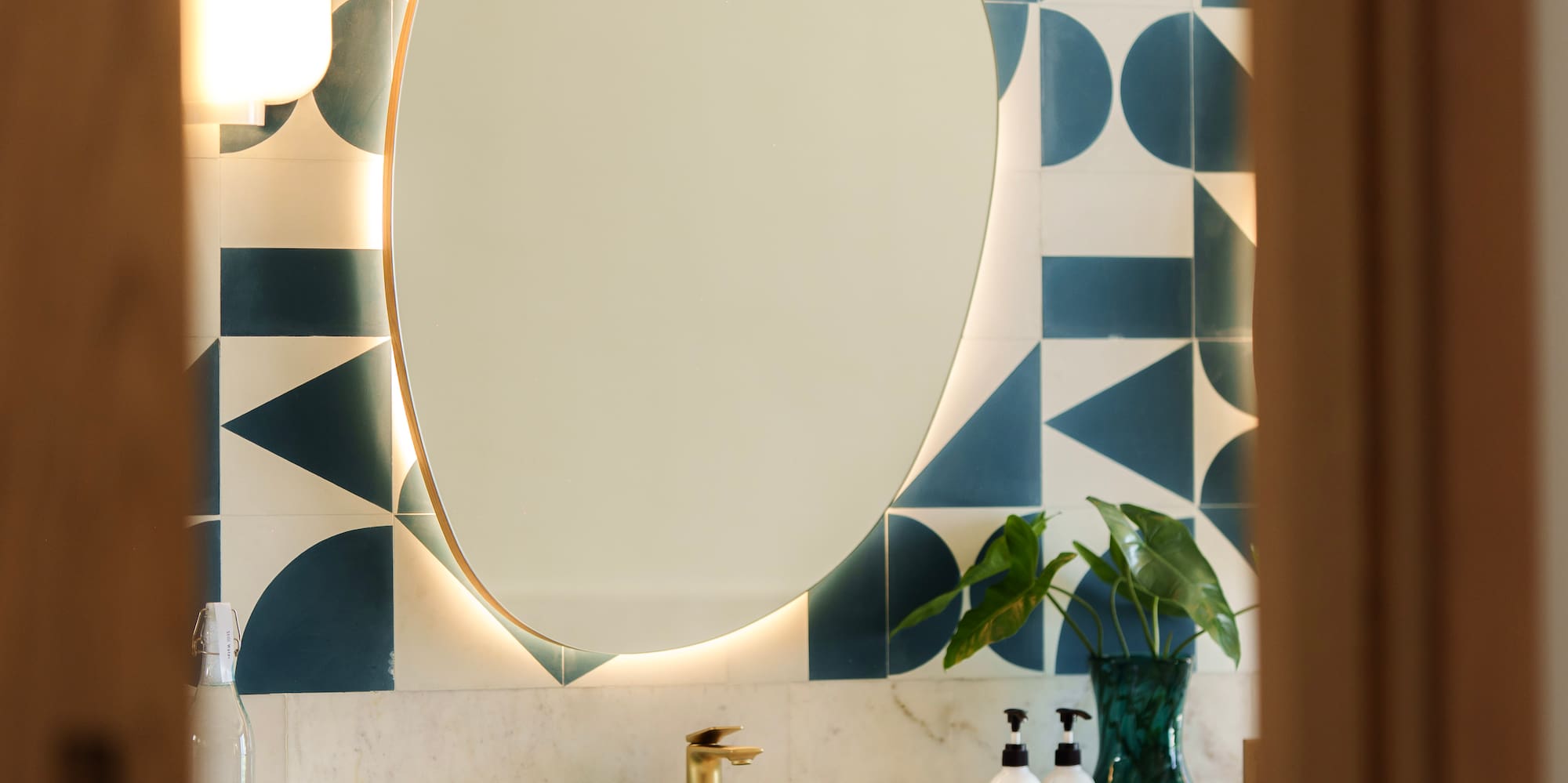 Modern bathroom vanity with backlit mirror, geometric teal tiles, and wood cabinet.