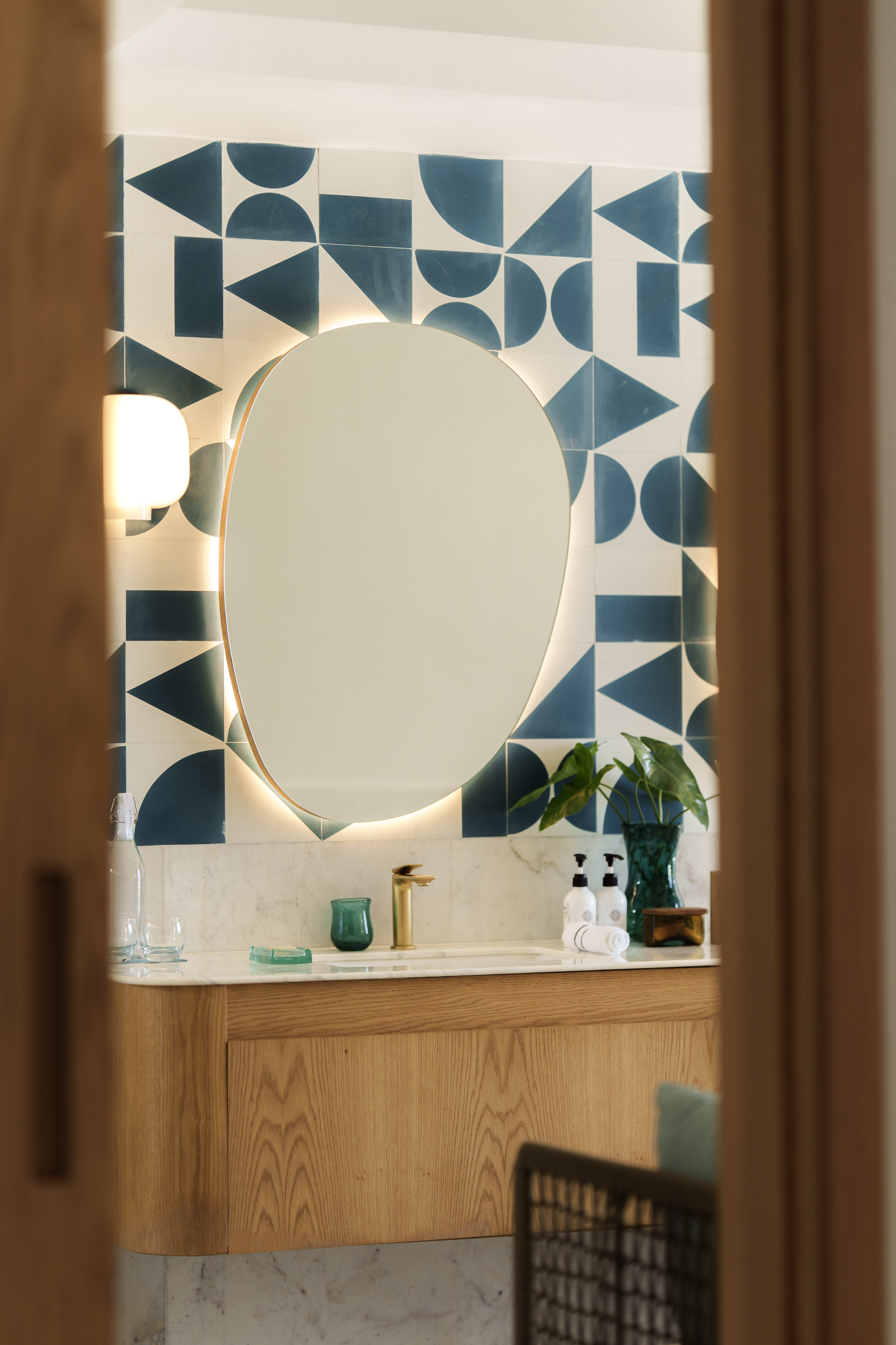 Modern bathroom vanity with backlit mirror, geometric teal tiles, and wood cabinet.