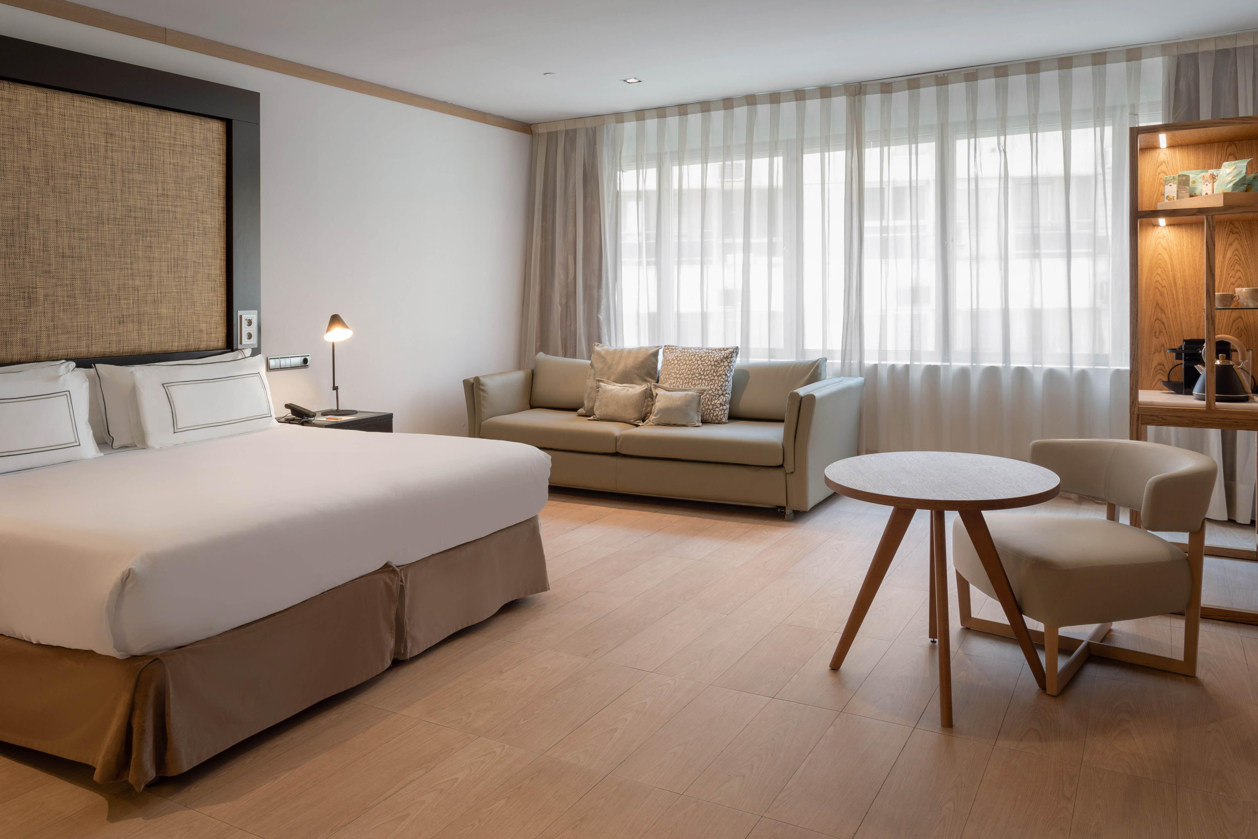 Habitación de hotel moderna con cama king-size, tonos neutros y ventanal.