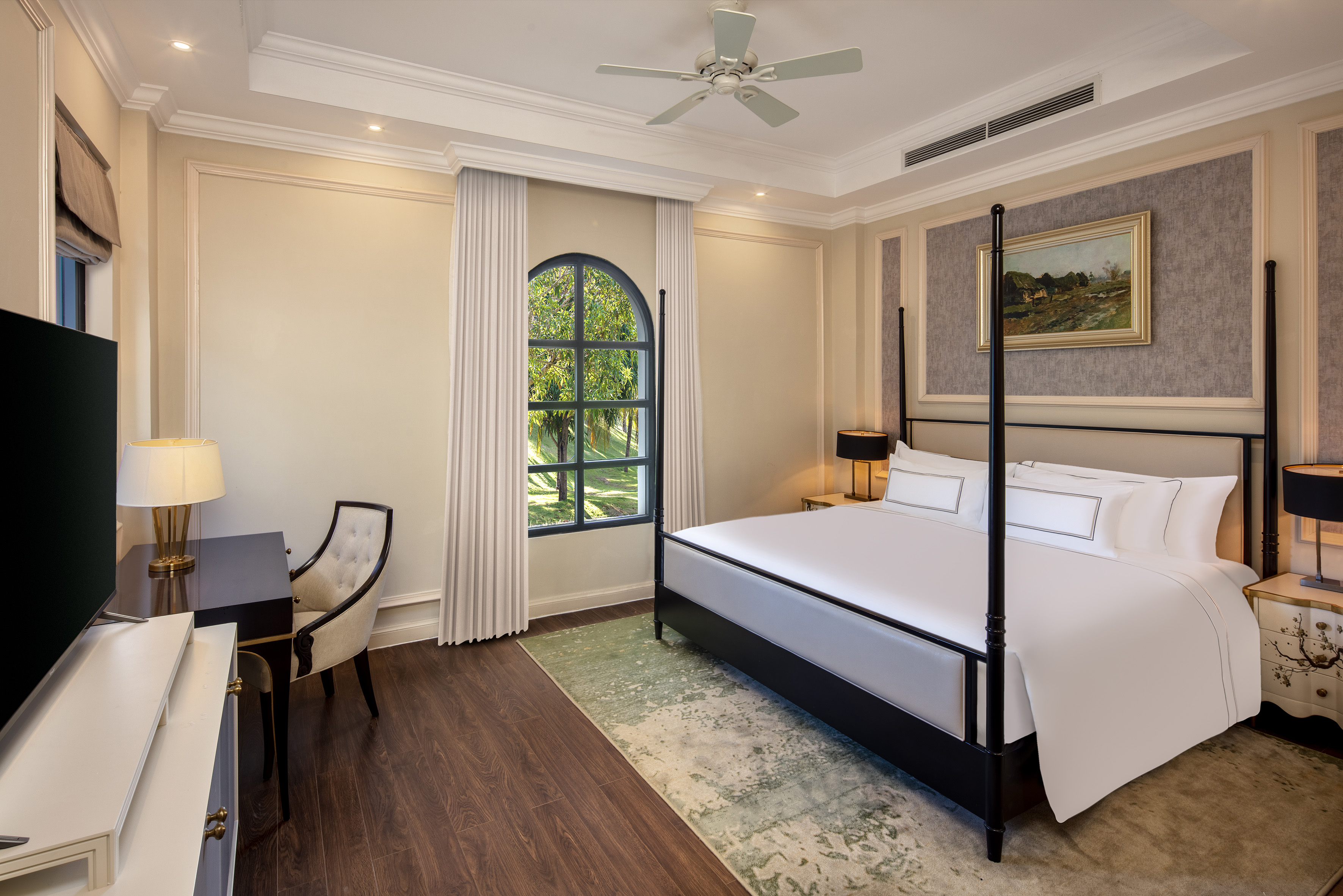 Luxury hotel bedroom with four-poster bed, arched window, and elegant decor.