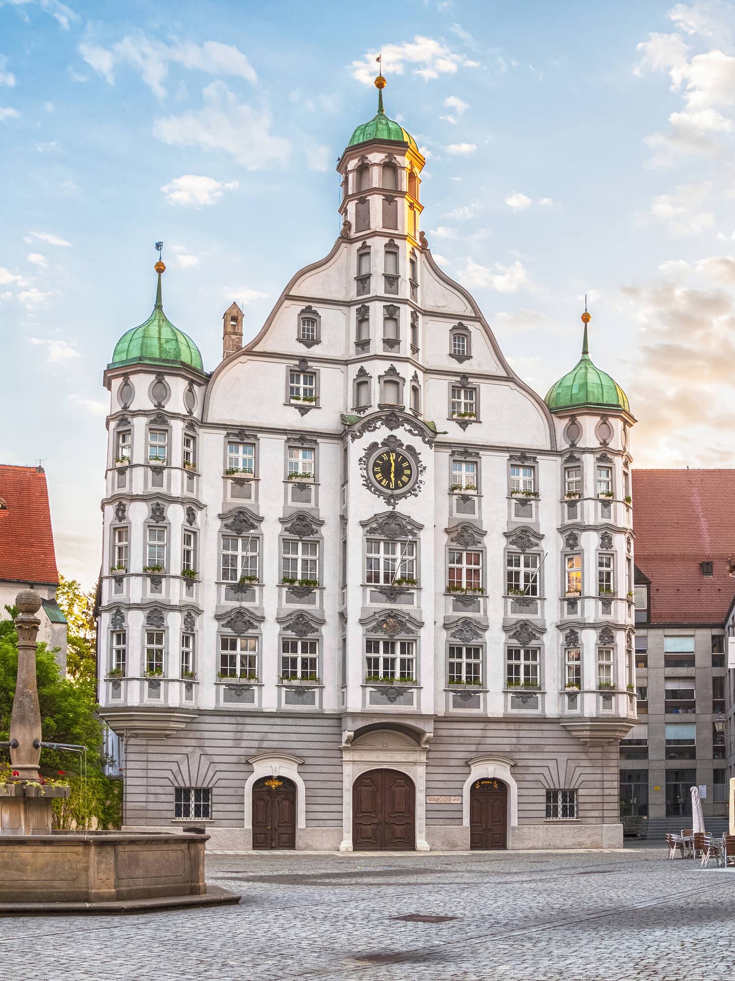 Historic German town hall with clock and green domes in cobblestone square.