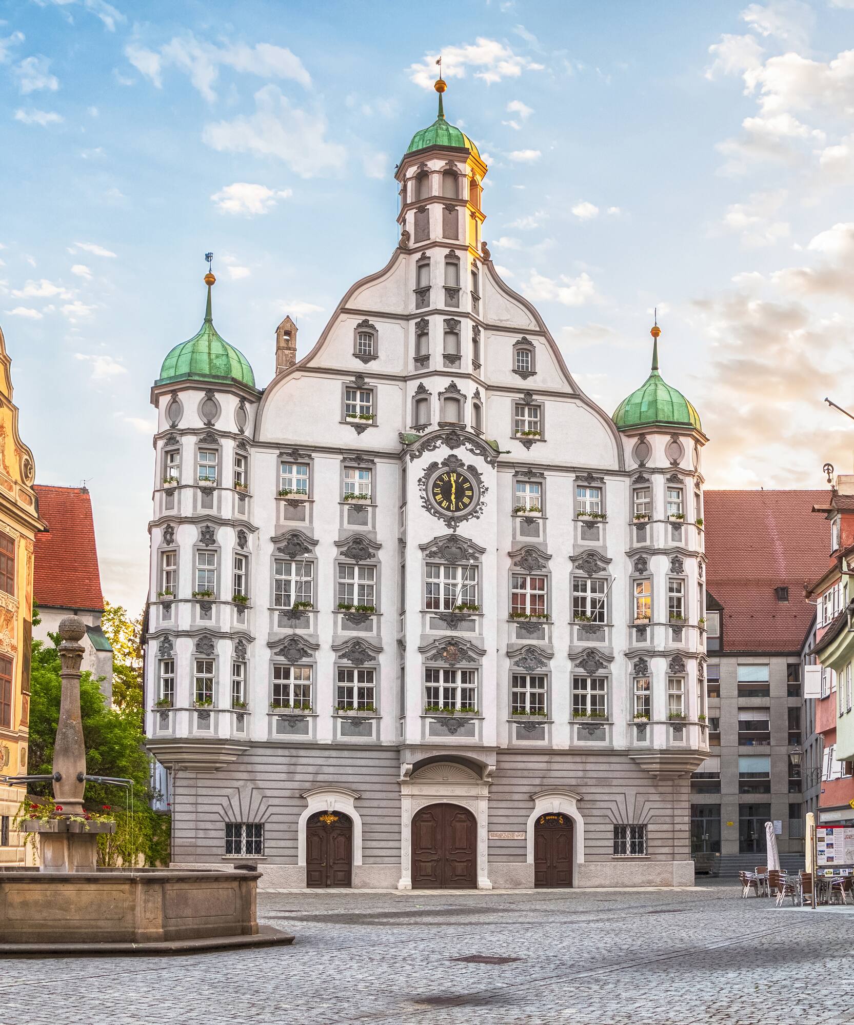 Historic German town hall with clock and green domes in cobblestone square.