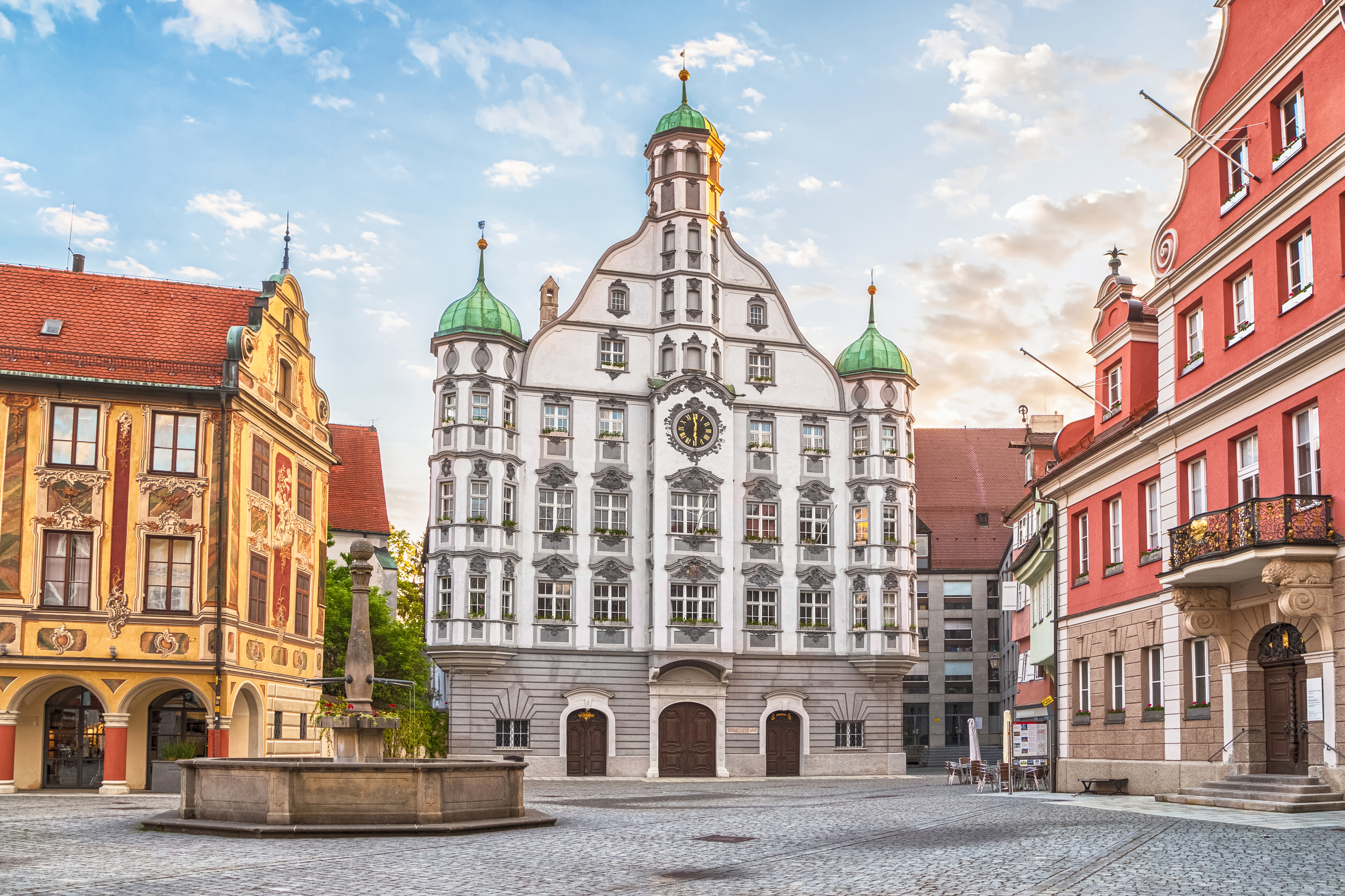 Historic German town hall with clock and green domes in cobblestone square.