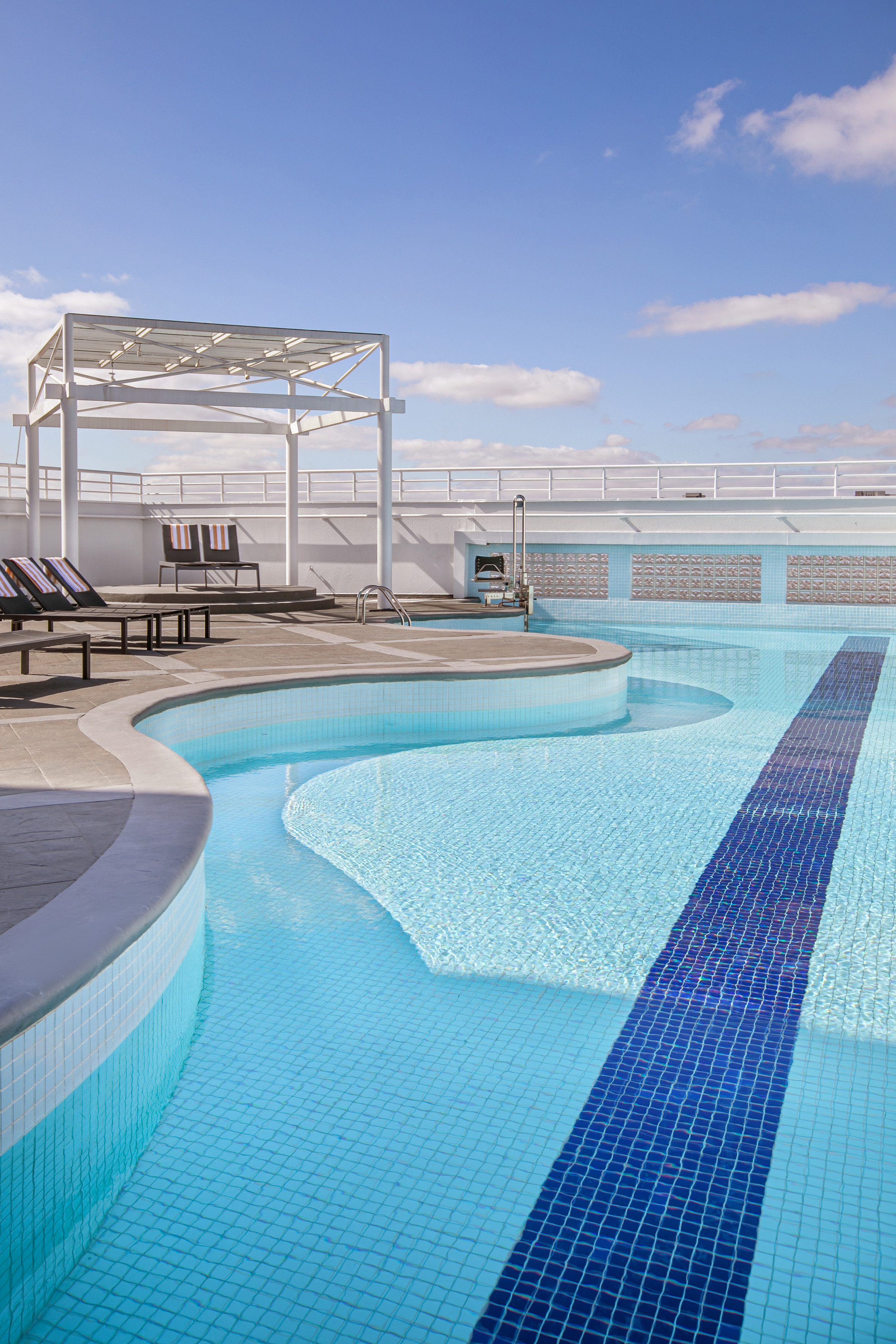 Modern outdoor pool with blue tiles, a lap lane, and resort lounge chairs.