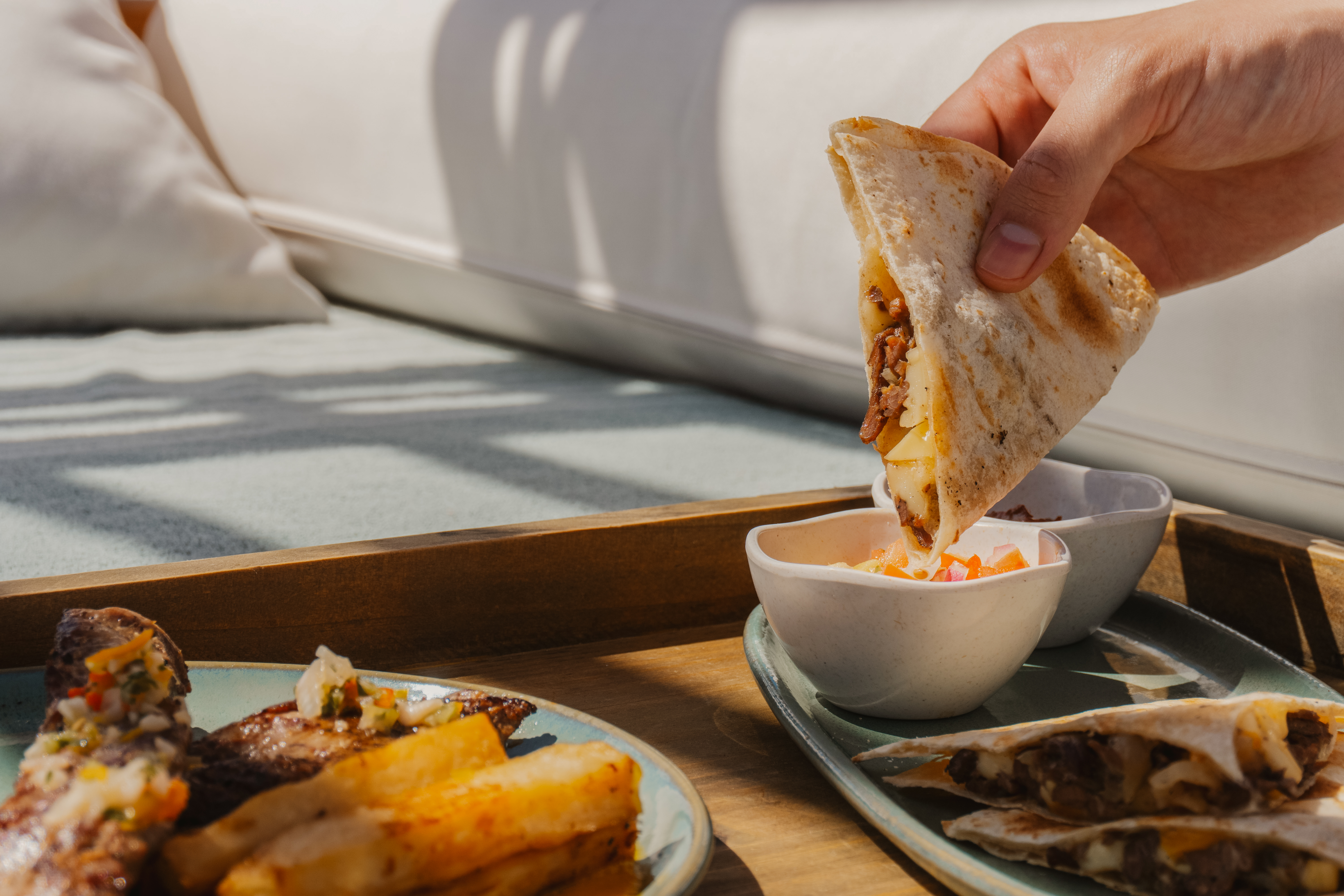 Hand dipping cheesy beef quesadilla into salsa. Steak, fries, and quesadillas.