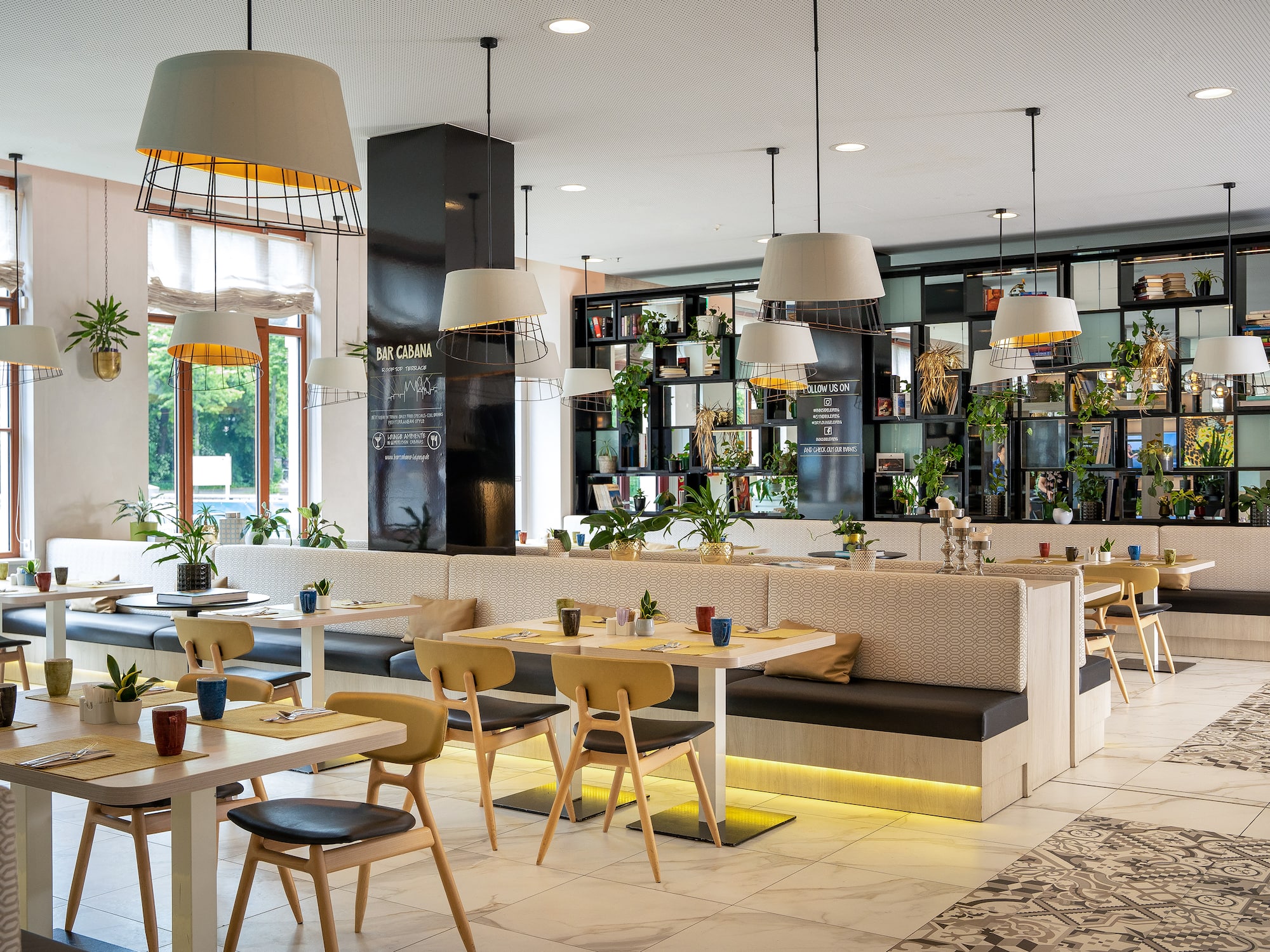 Bar Cabana: moderno restaurante con mesas, bancos, plantas y lámparas.