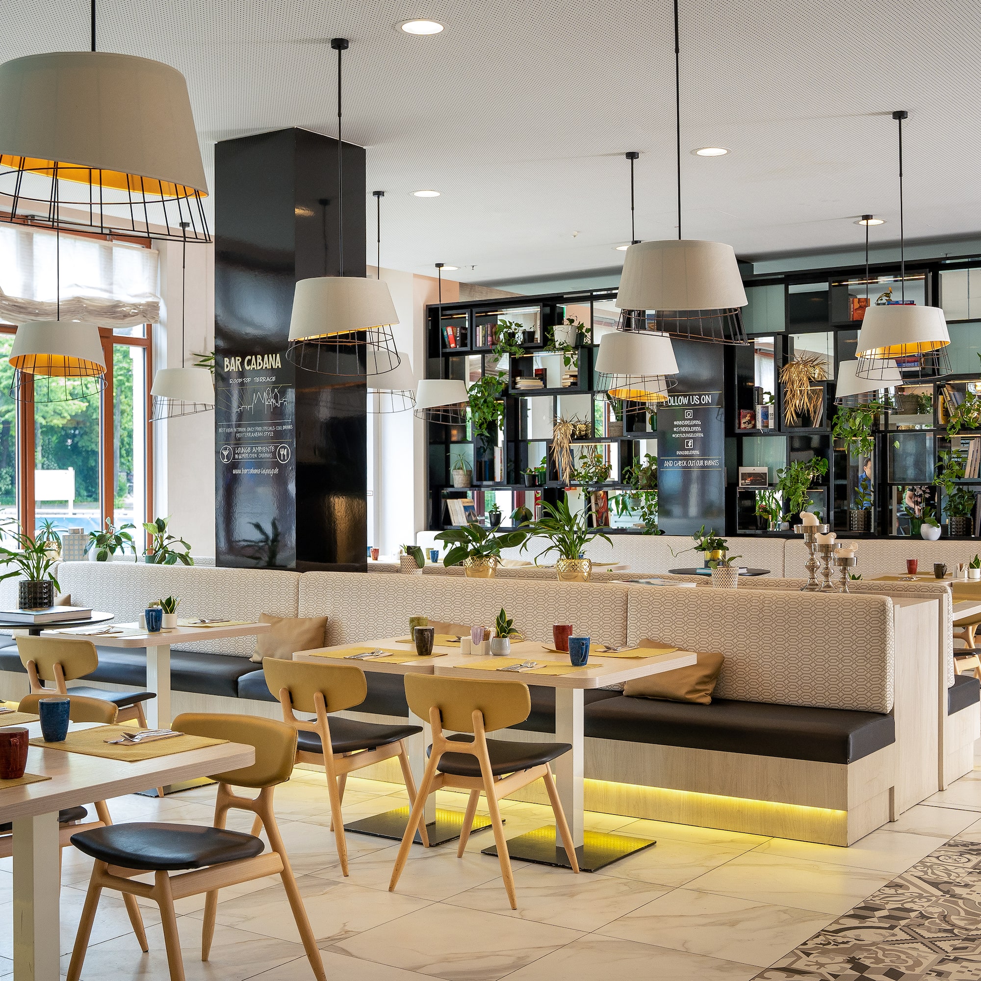 Bar Cabana: moderno restaurante con mesas, bancos, plantas y lámparas.