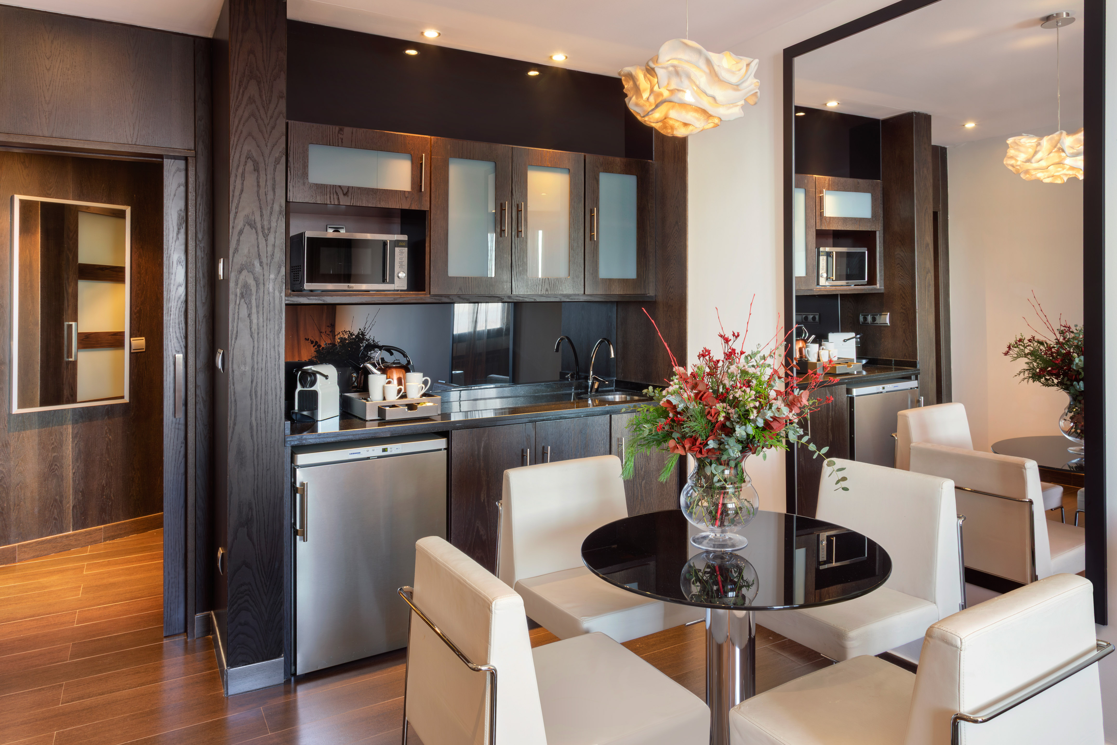 Modern hotel kitchenette with dark wood, stainless appliances, and dining table.
