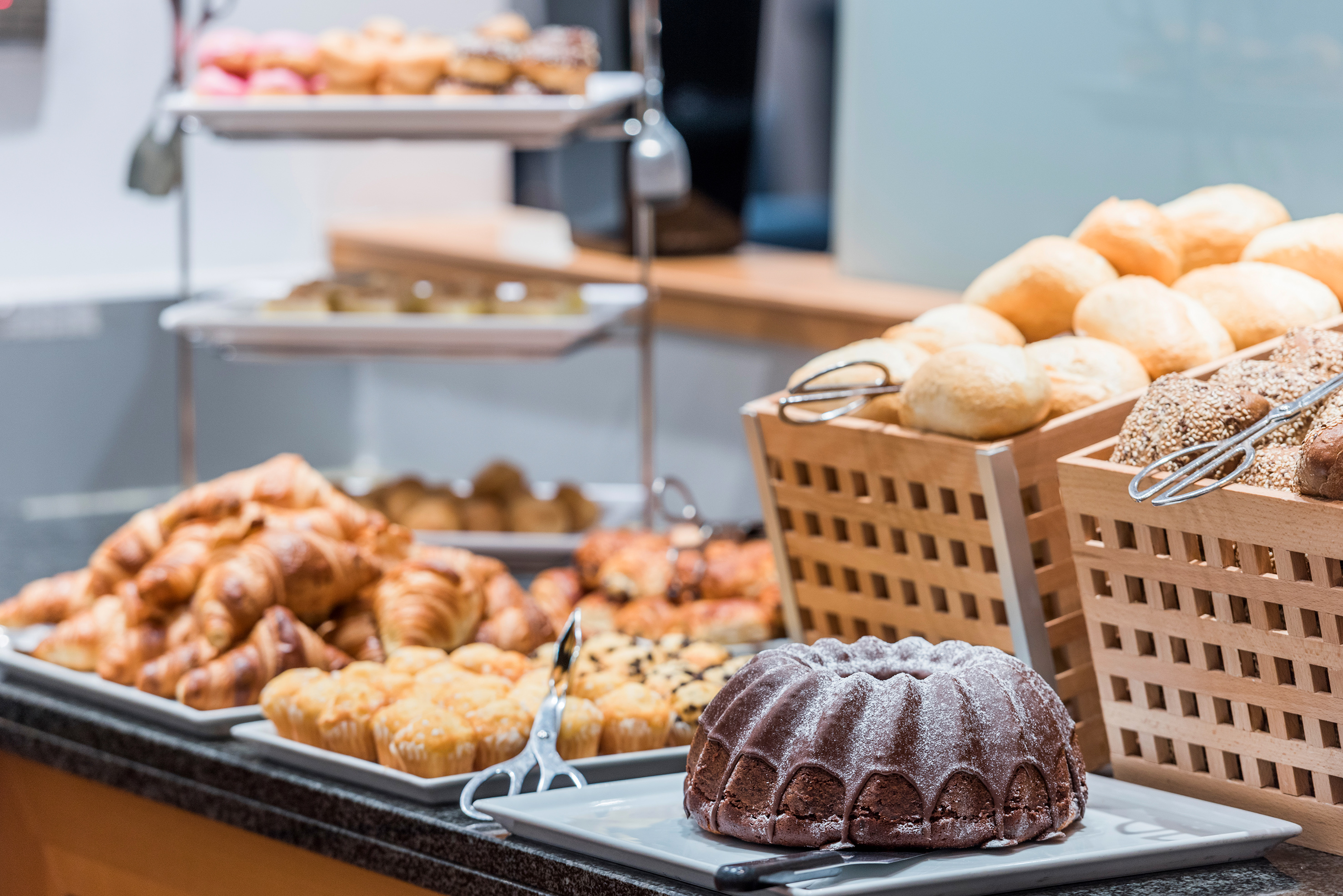 Hotel breakfast buffet with chocolate bundt cake, croissants, muffins, and bread rolls.