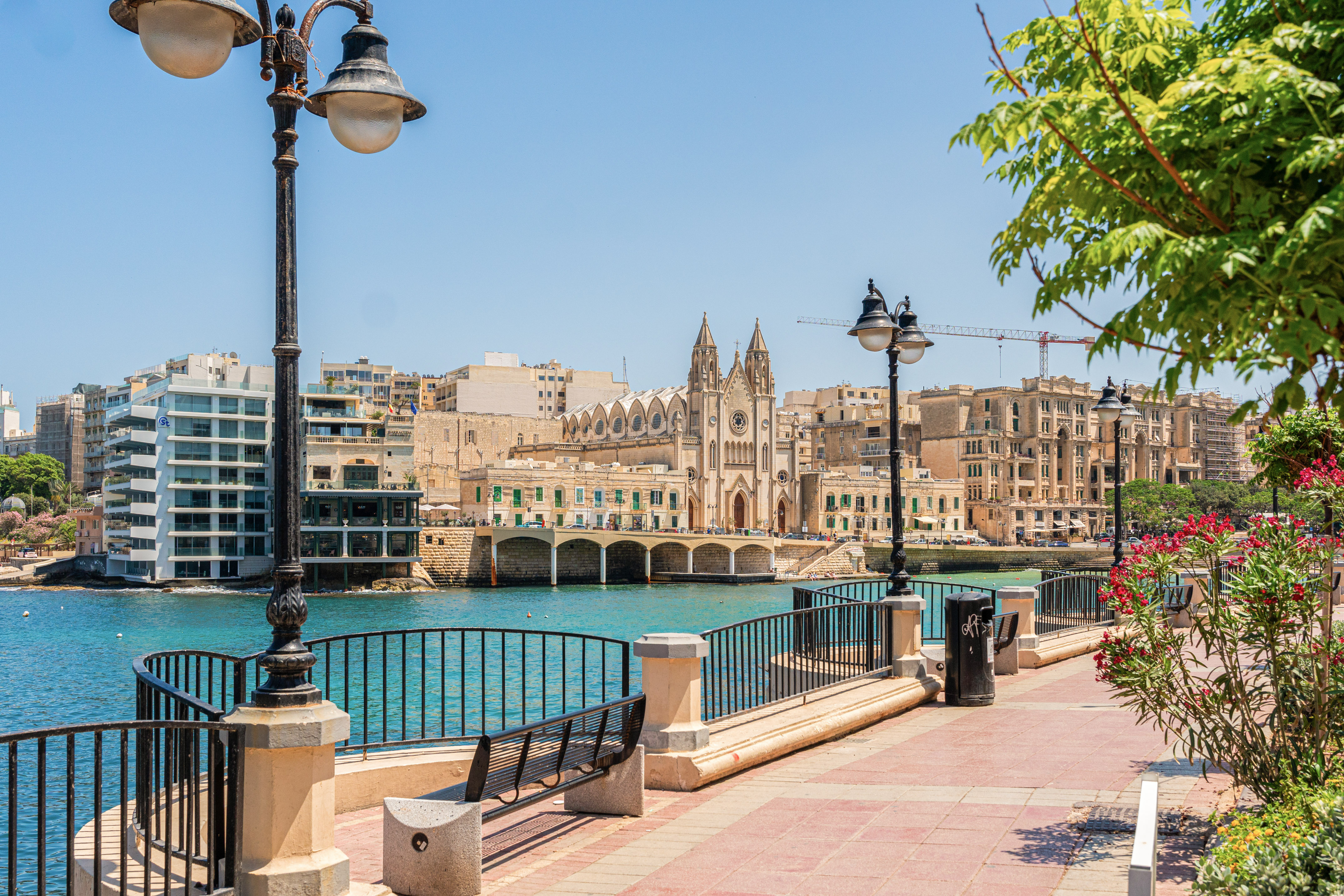 St. Julian's Balluta Bay promenade with Neo-Gothic church and clear blue sea.