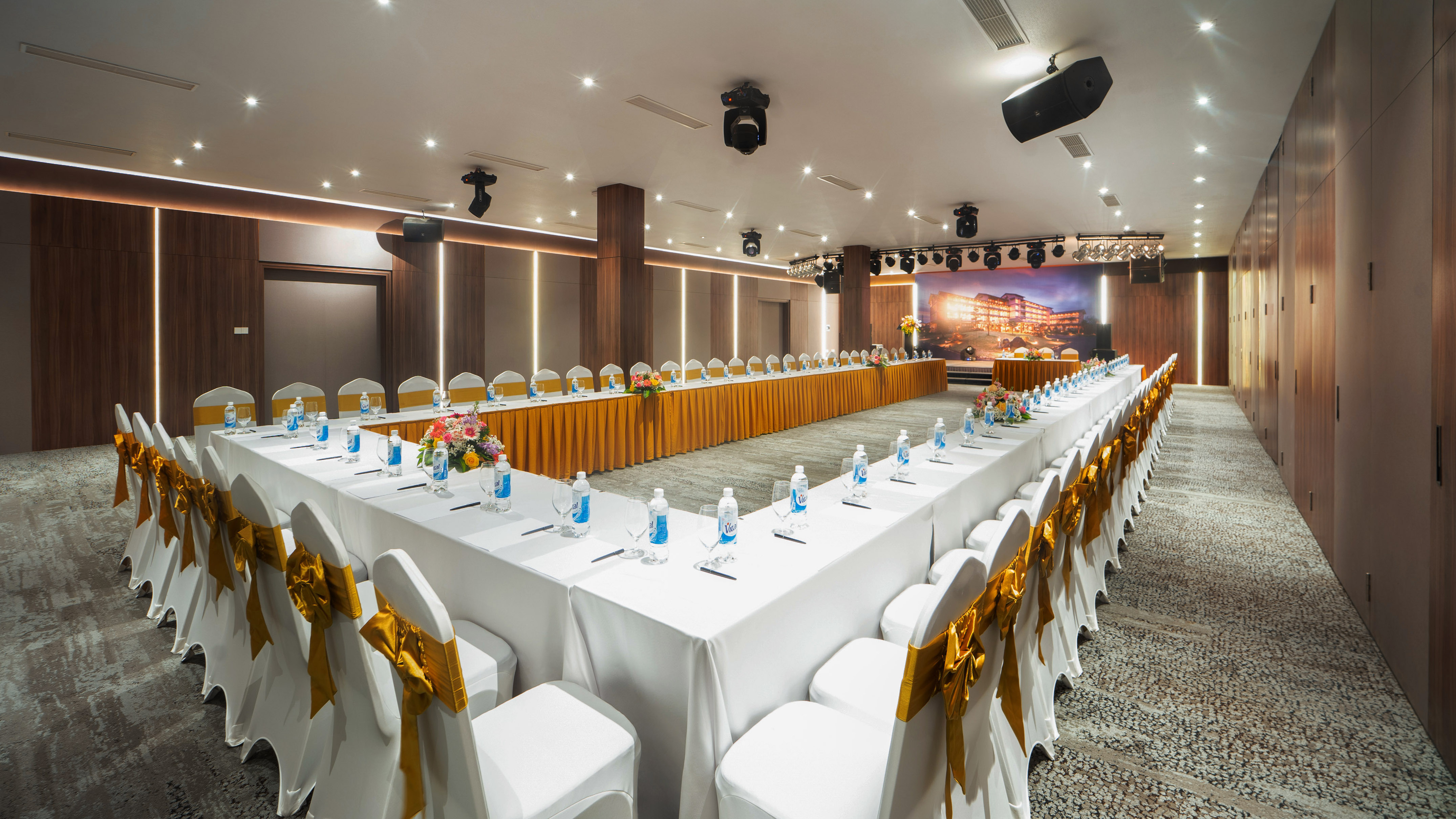 Modern U-shape conference room with golden chairs, stage, and screen.